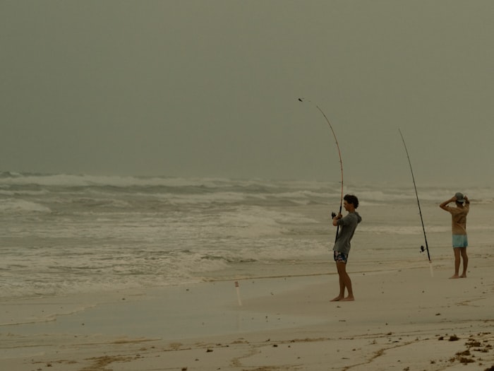 Two anglers surf fishing from a sandy ocean beach