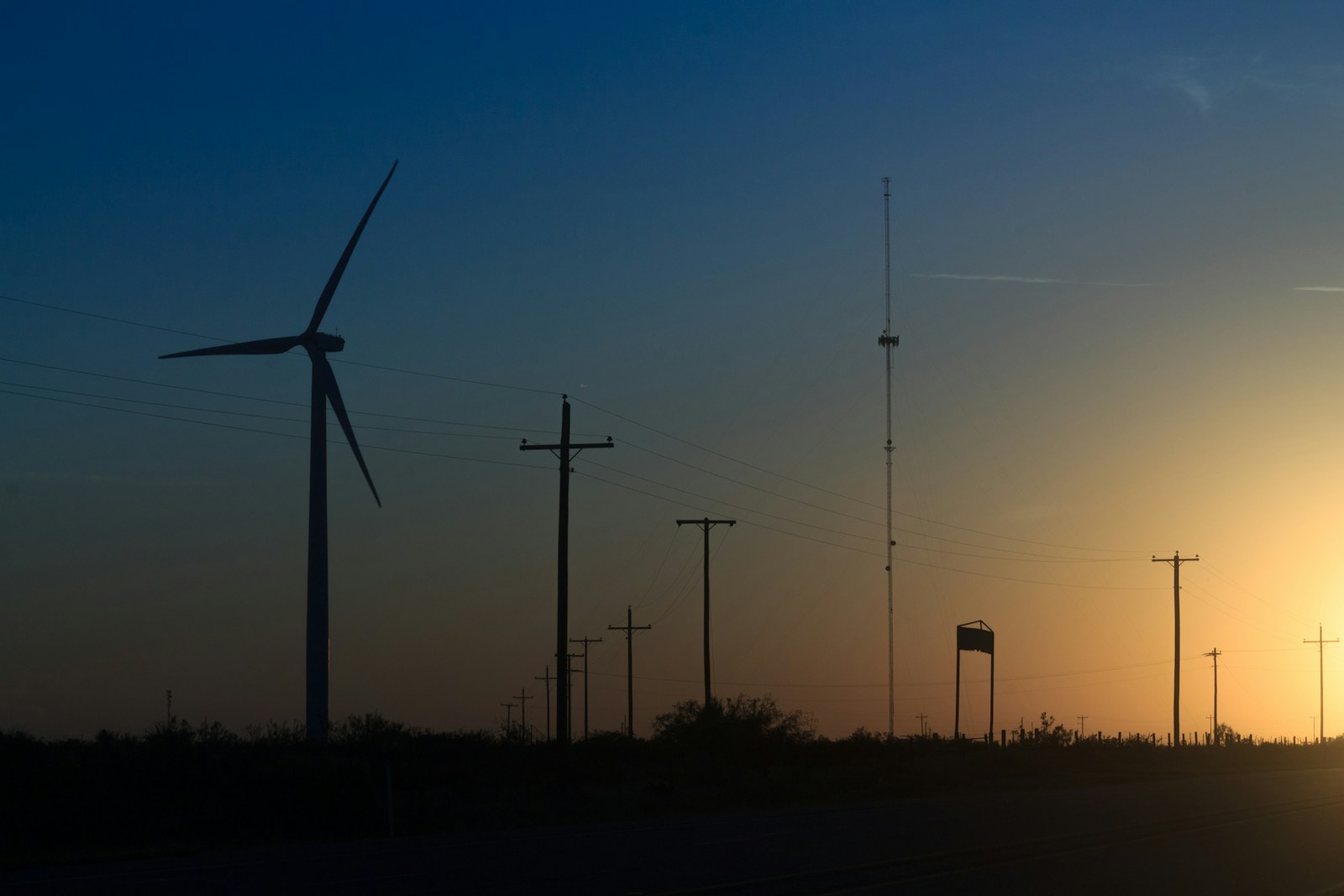 A wind turbine and power poles silhouetted against a colorful sunset