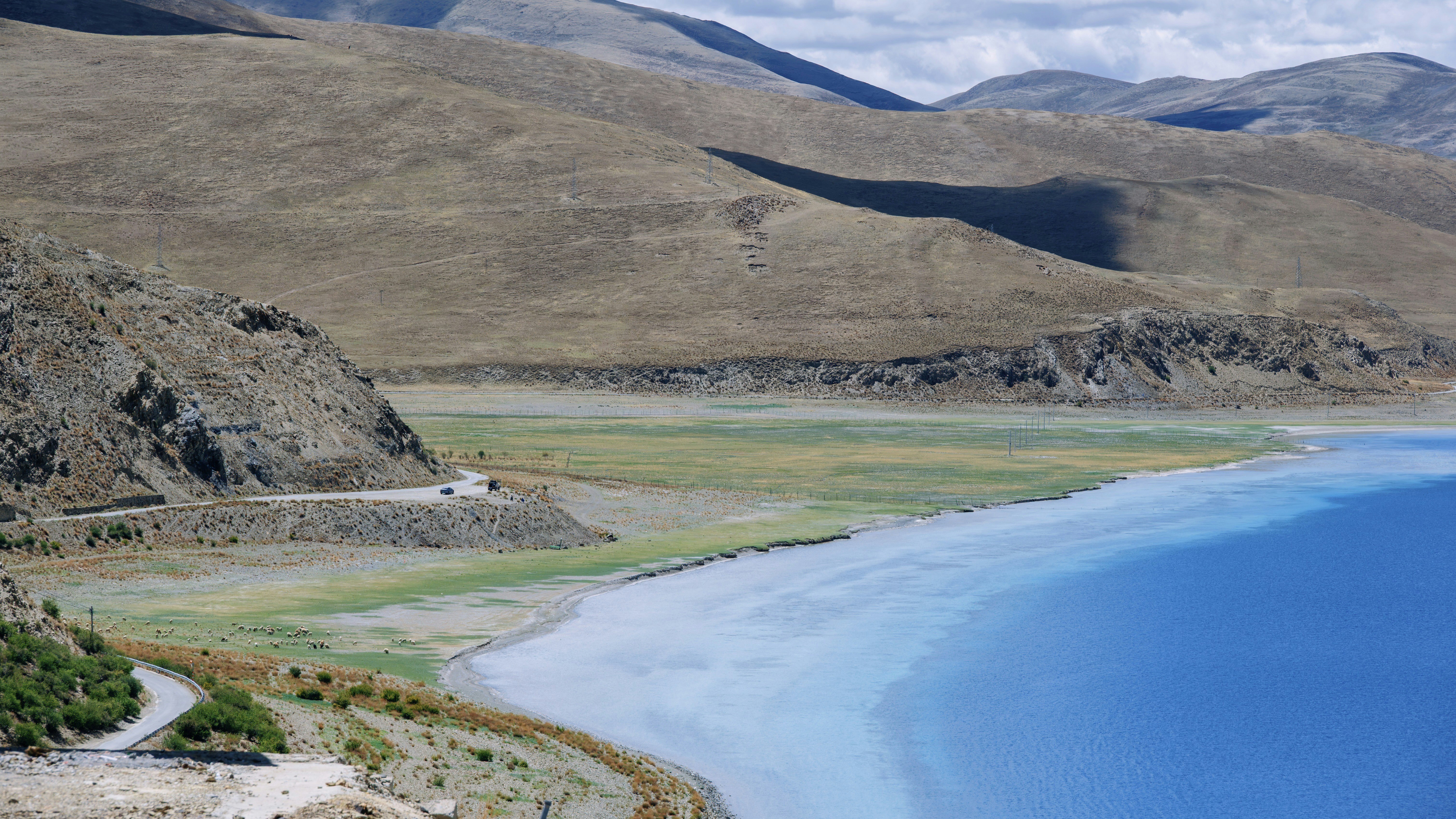 Vibrant blue lake with arid mountains and a winding road.