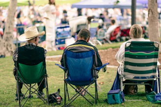 Three people sitting in folding chairs at an outdoor event.