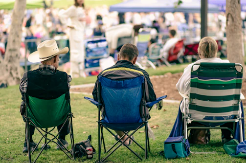 Three people sitting in folding chairs at an outdoor event.