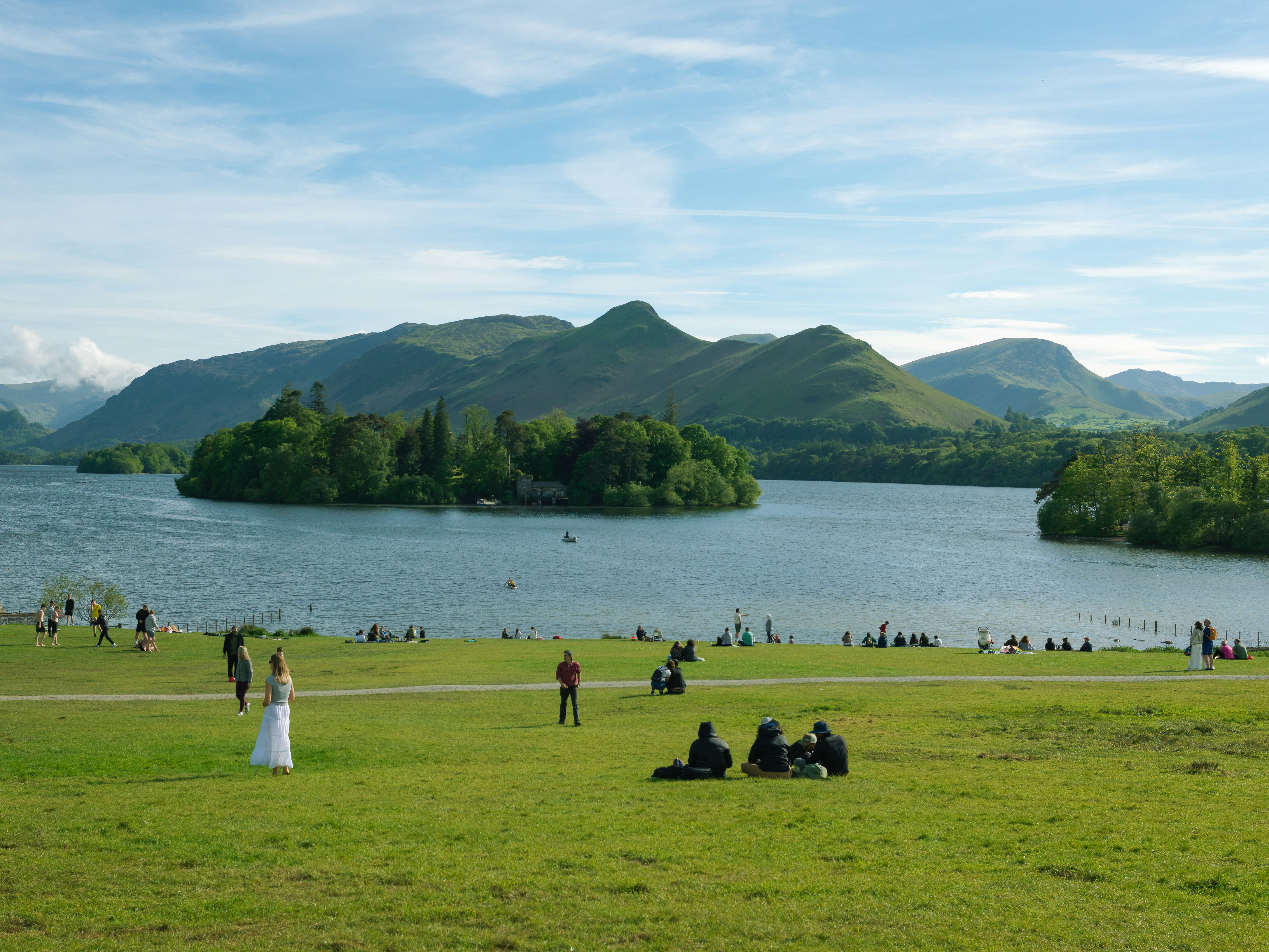 People relaxing by a lake with mountains and an island.