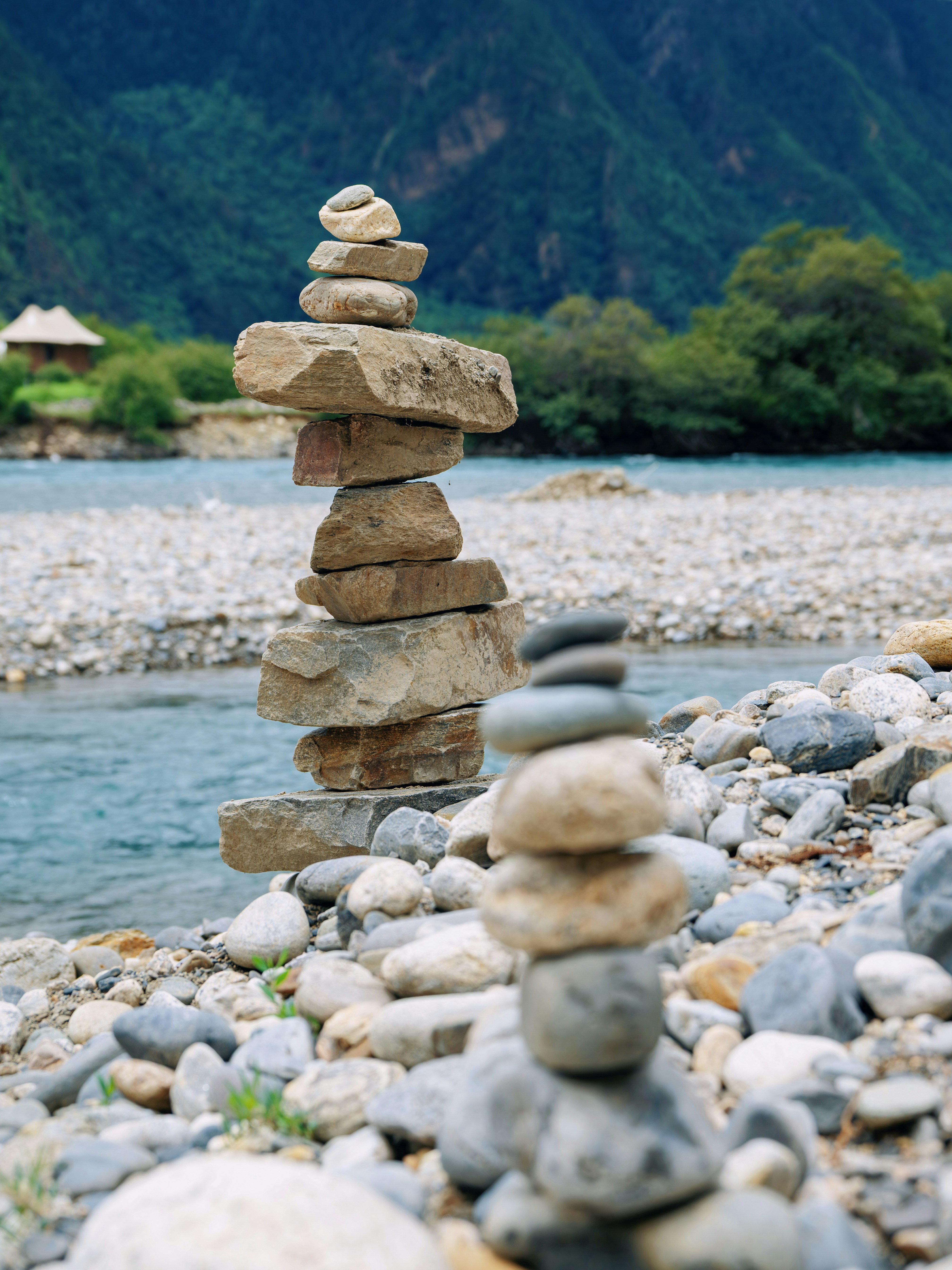 Two balanced rock stacks on a riverbank with mountains.