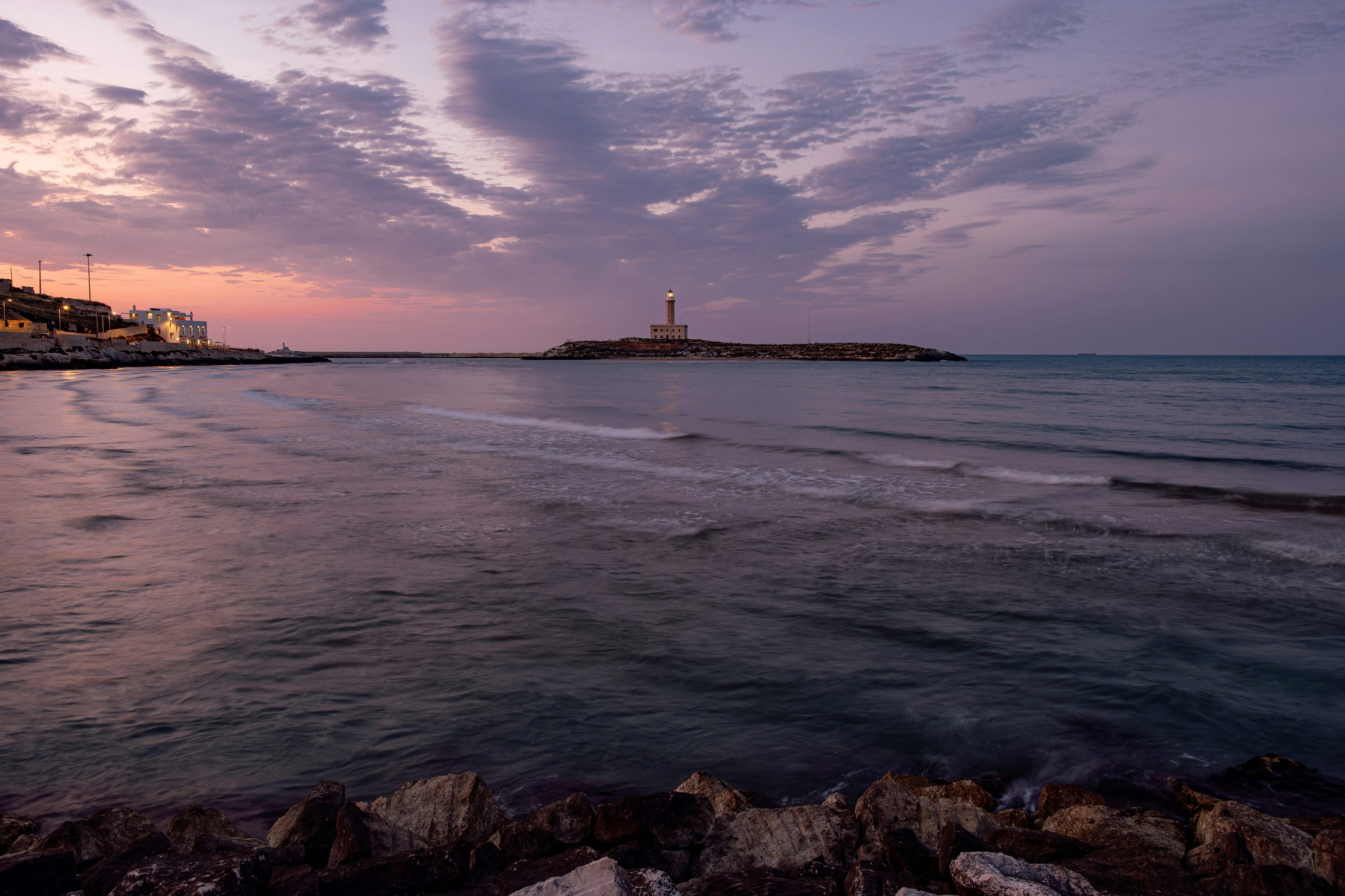 Distant lighthouse against a vibrant sunset sky over the ocean