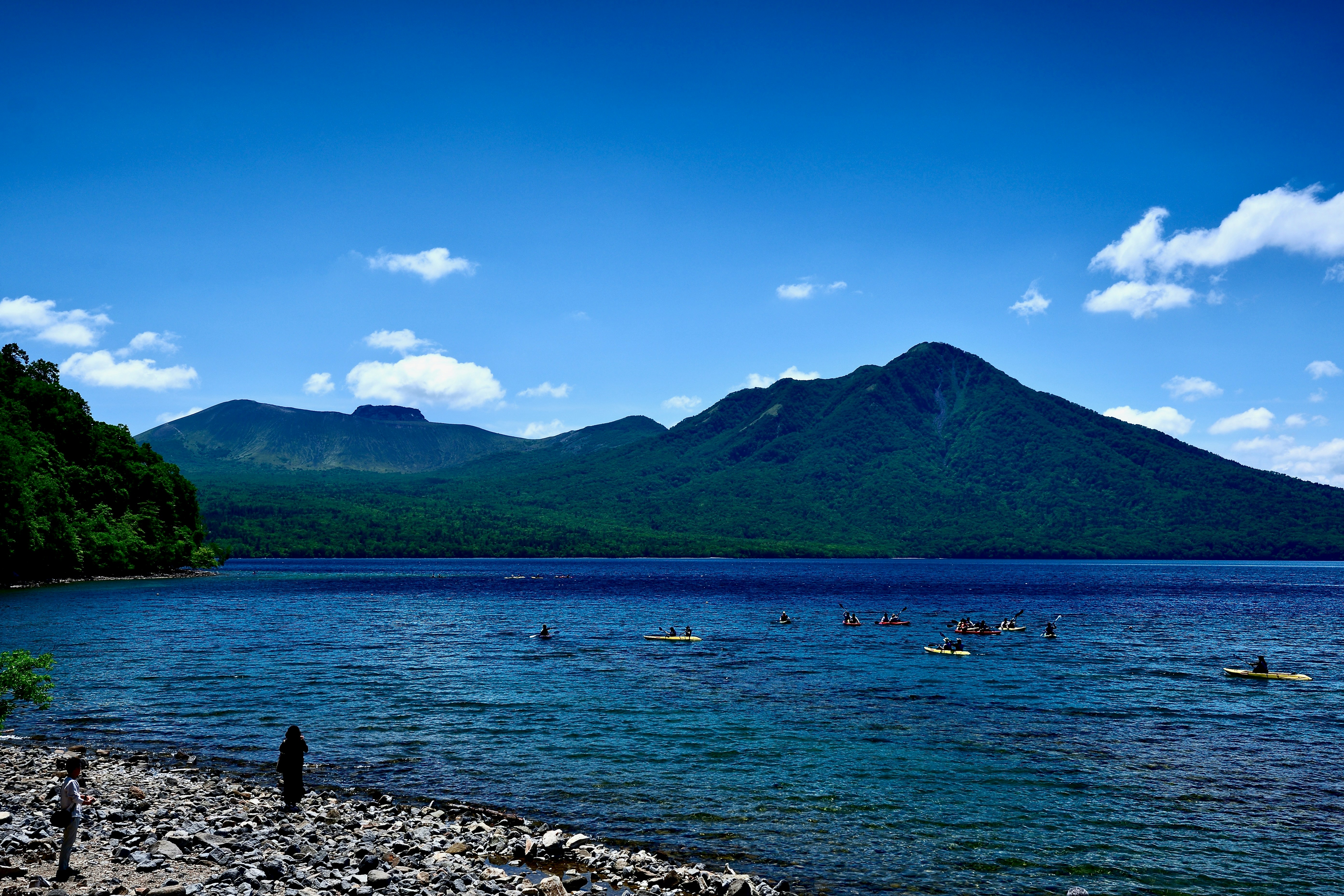 Scenic lake with distant mountains and people kayaking.