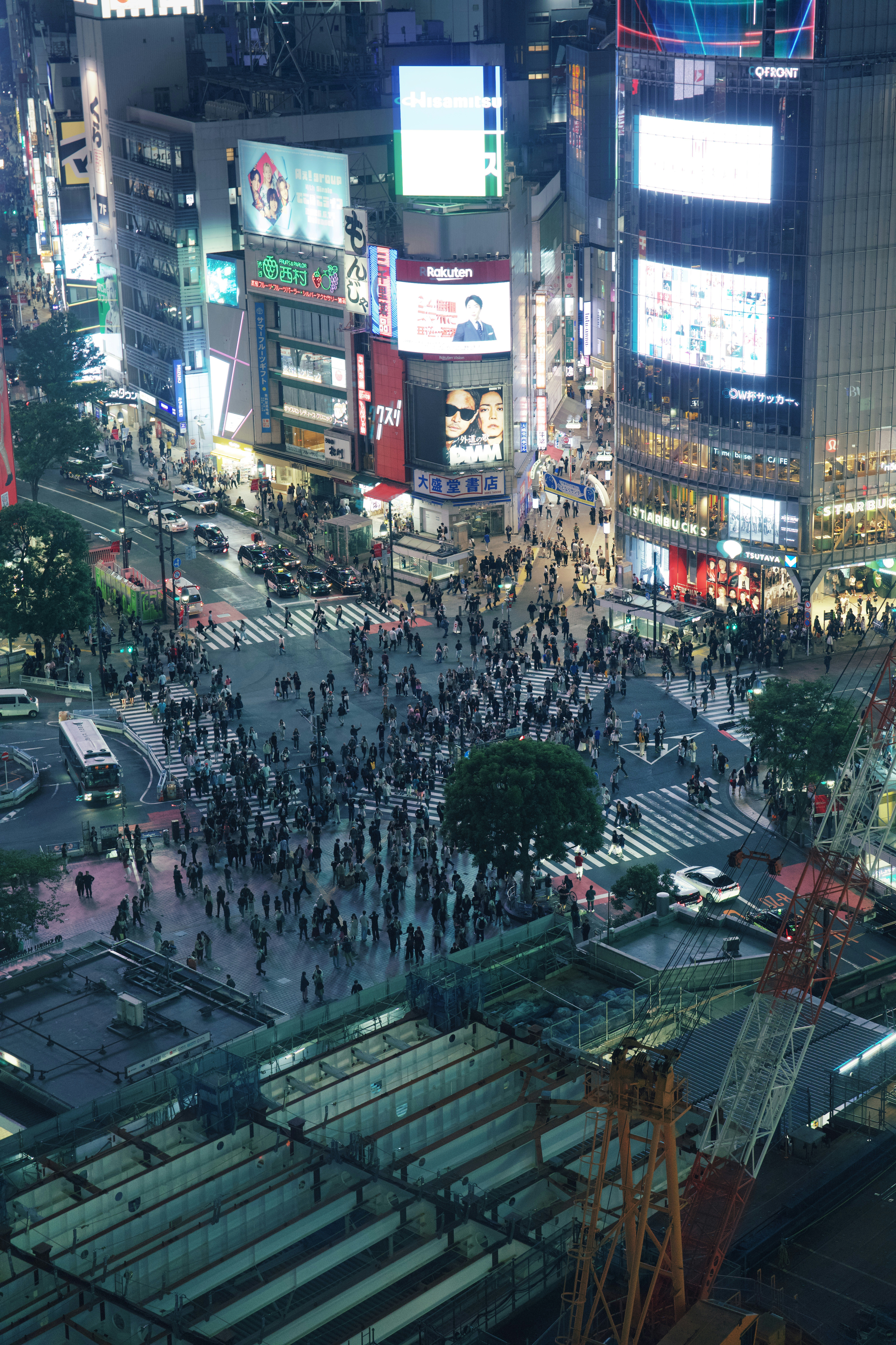 Crowds cross a vibrant city intersection surrounded by bright signs.