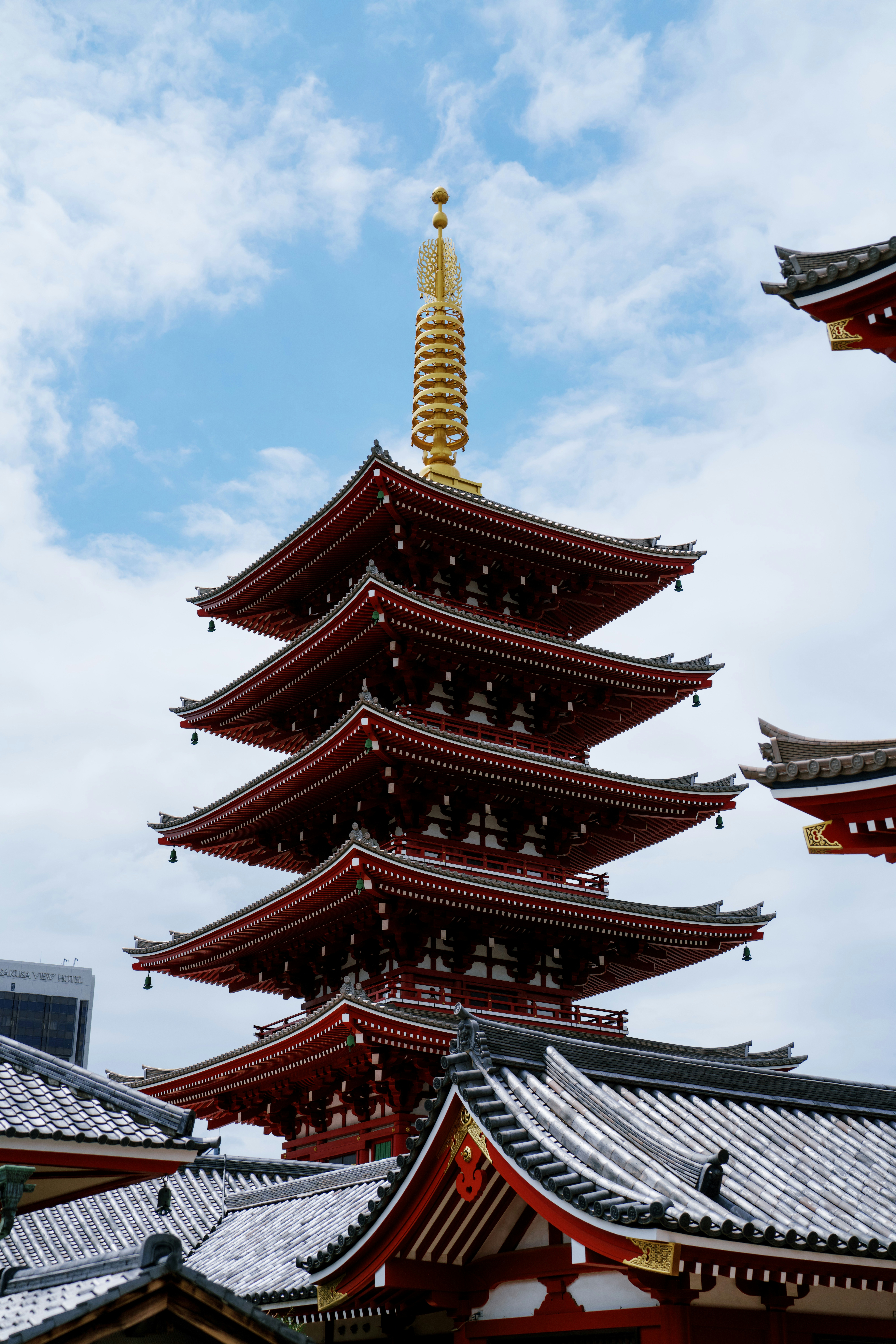 Red japanese pagoda with golden spire under a blue sky.