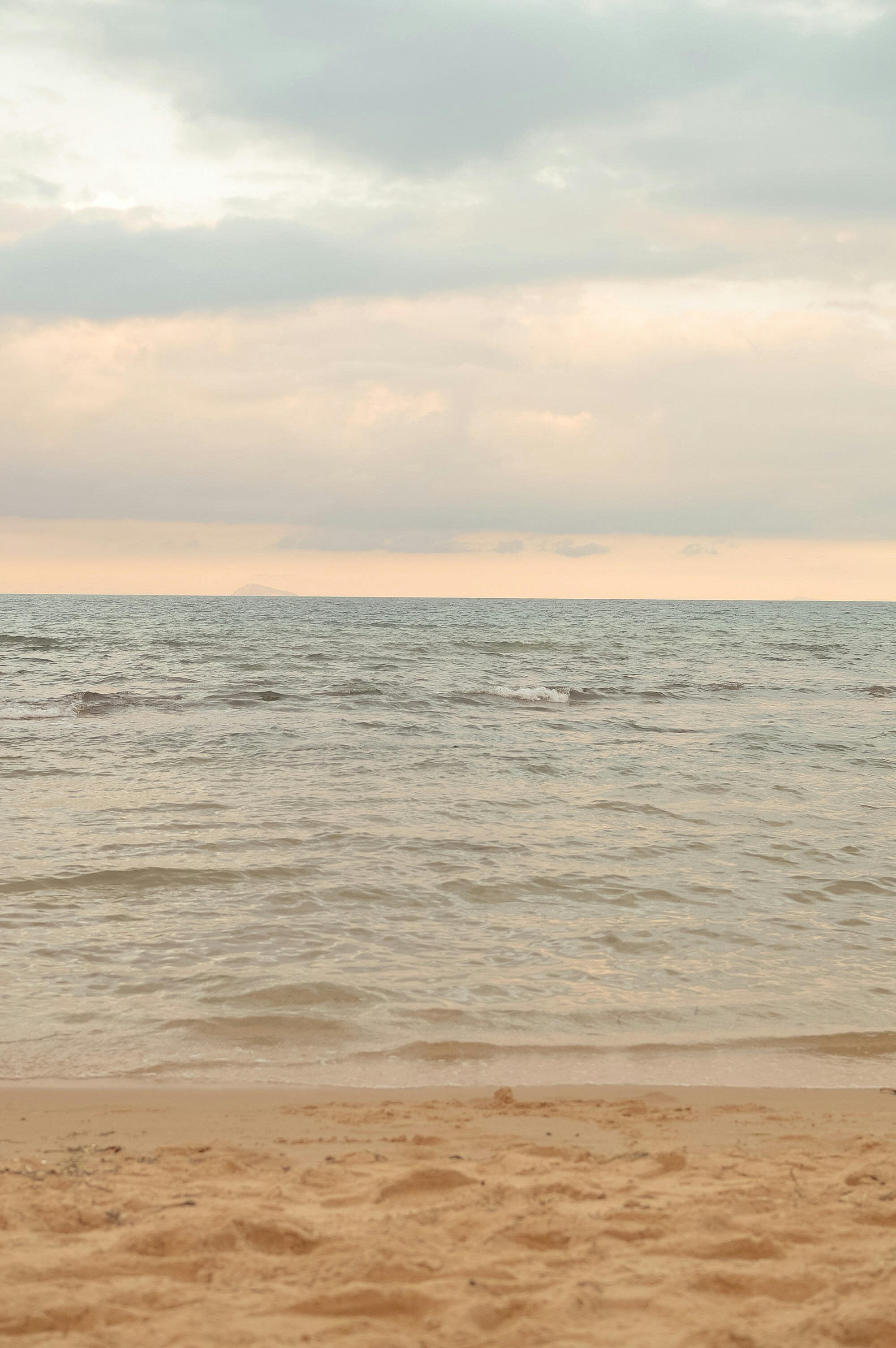 Sandy beach, calm ocean, and soft cloudy sky.