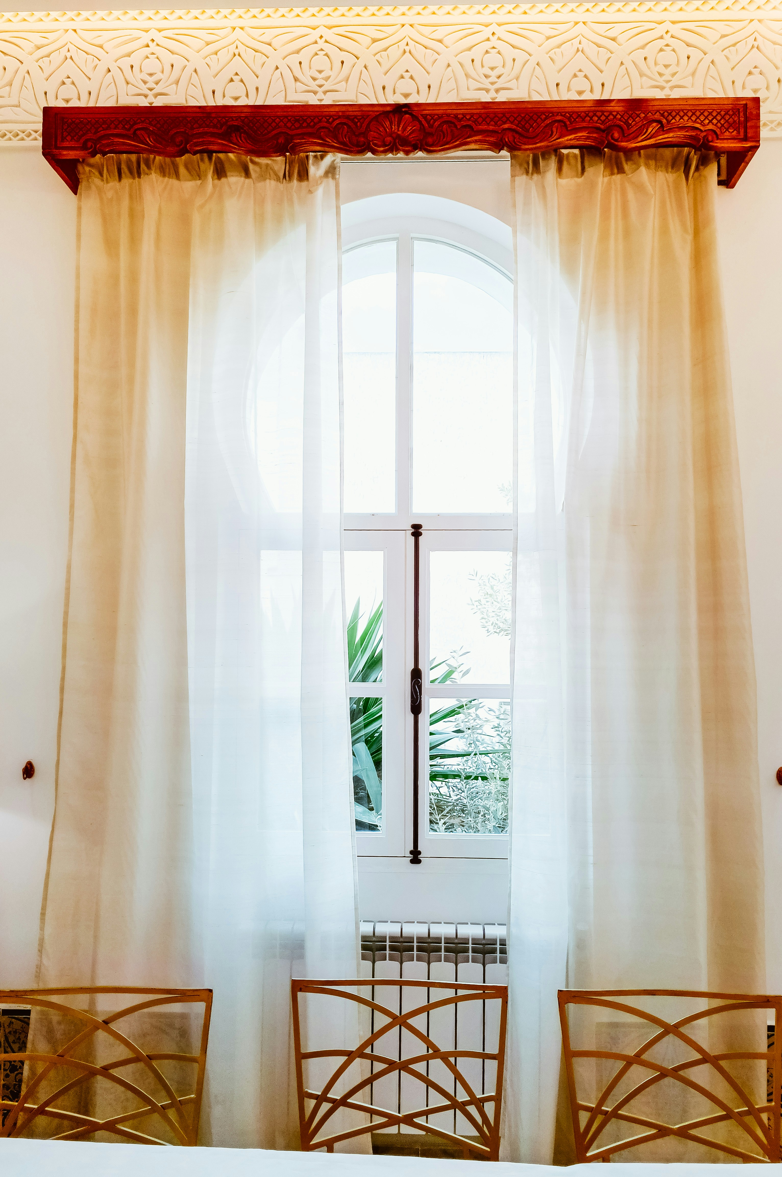 Bogenfenster mit transparenten Vorhängen und kunstvollen Stühlen.