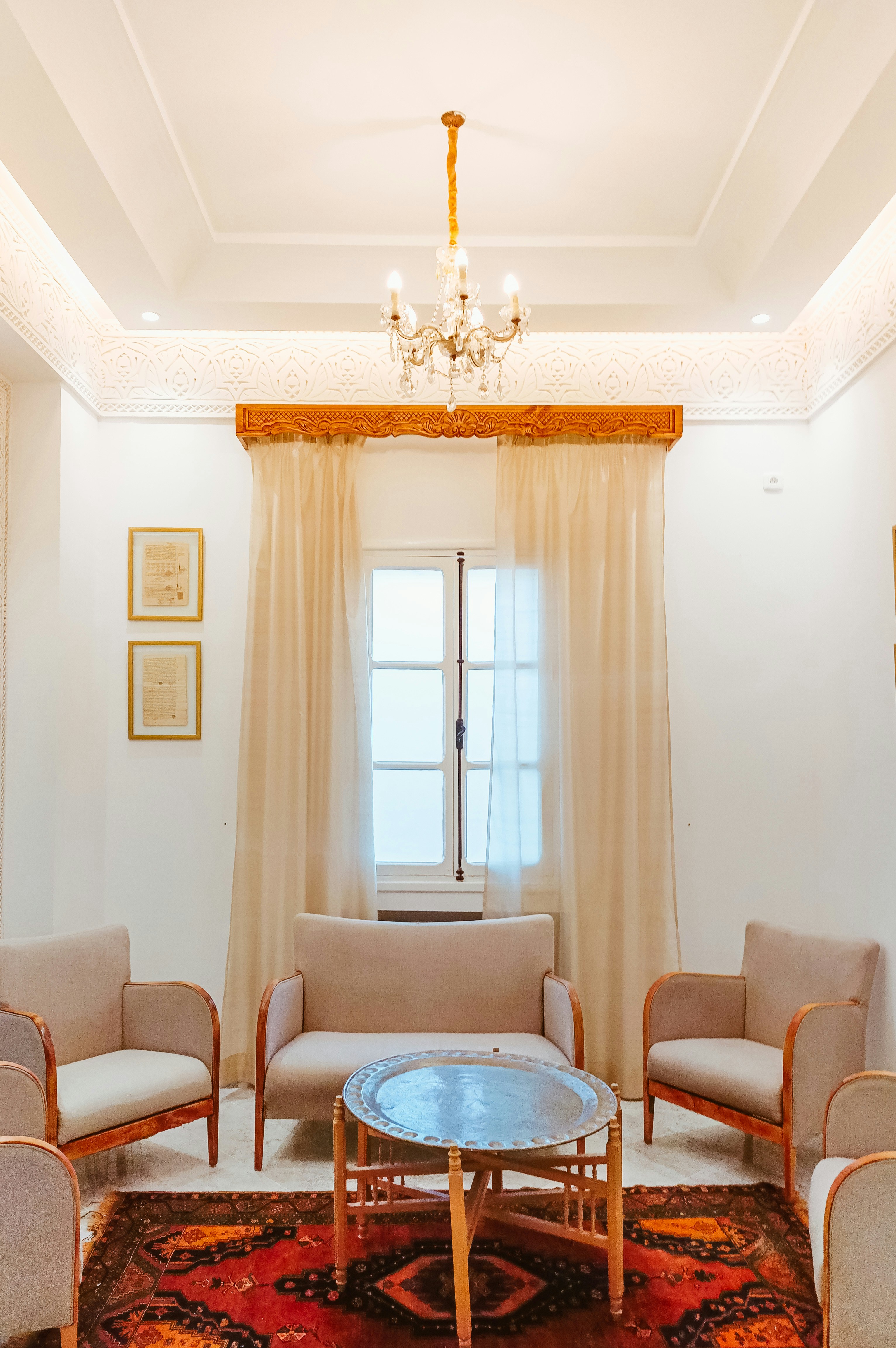 Eleganter Raum mit Kronleuchter, Sofa, Stühlen, Fenster und gemustertem Teppich.