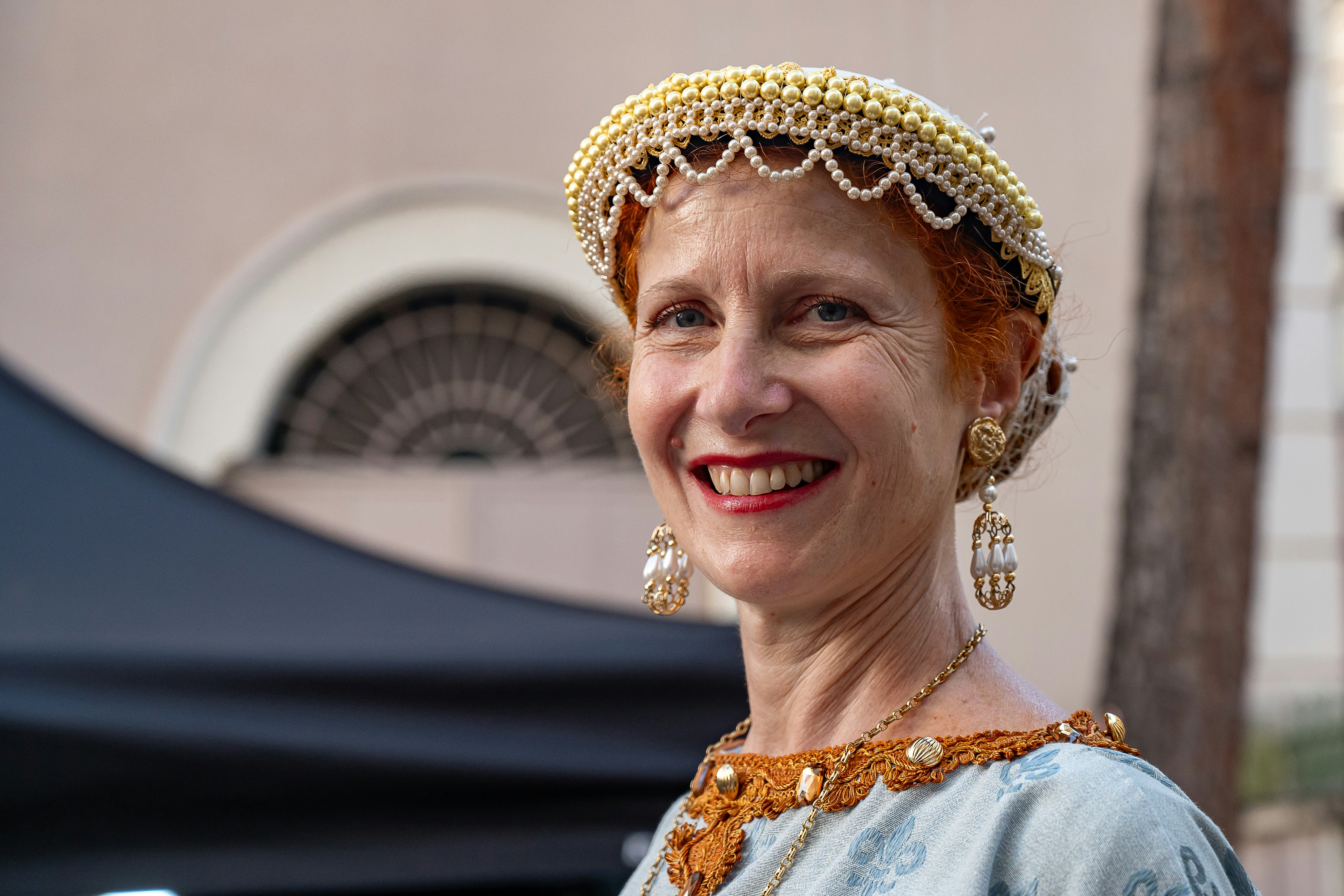 Eine lächelnde Frau in historischer Kleidung mit Perlenkopfschmuck.