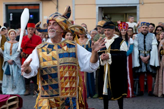 Jester in colorful medieval costume entertains a costumed crowd.