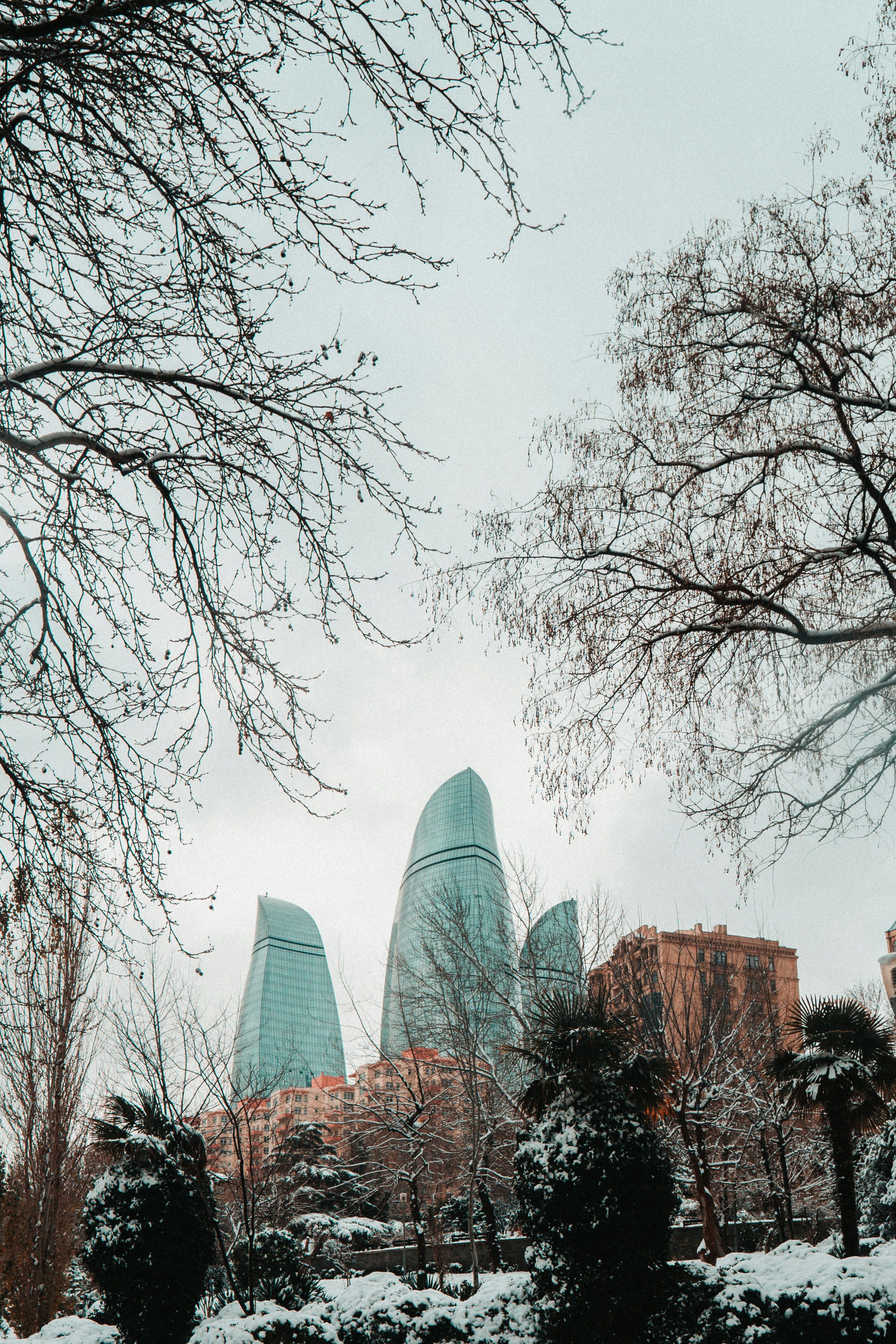 Flame towers rise above a snow-covered park with bare trees.