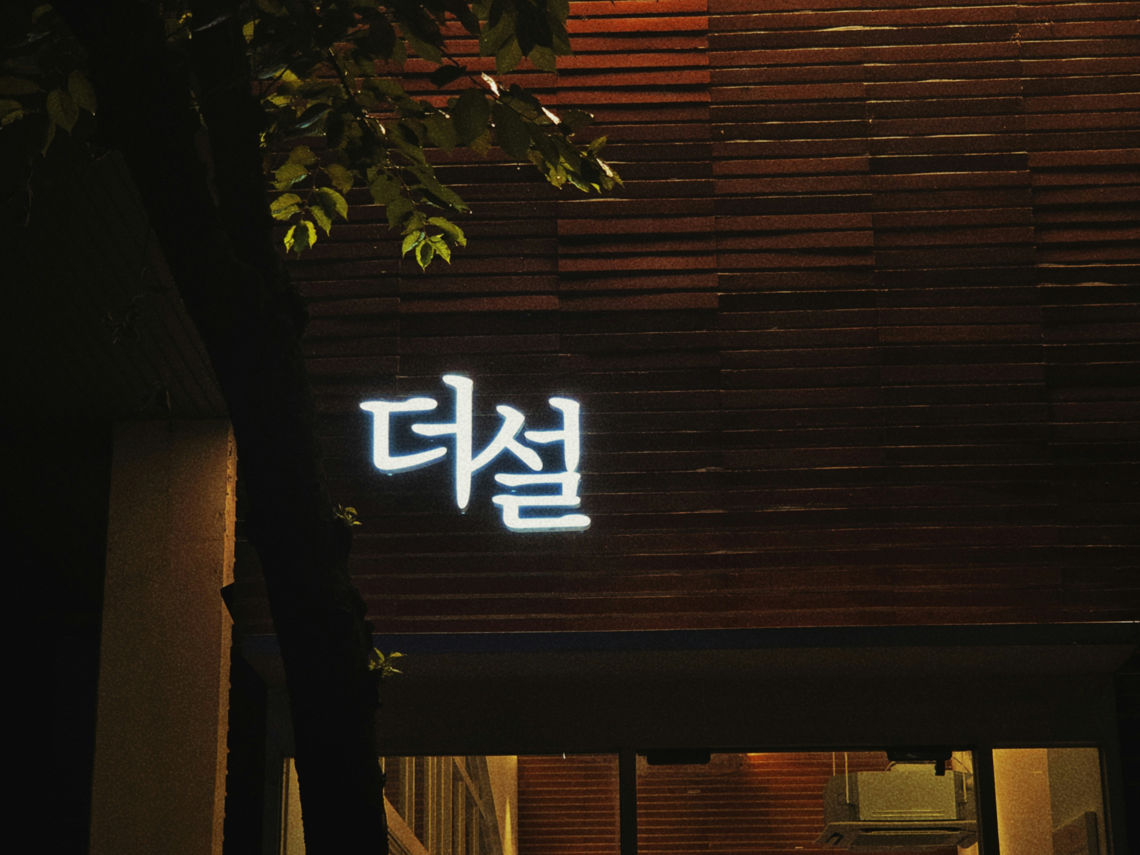 A glowing korean sign "더설" on a dark wooden building.