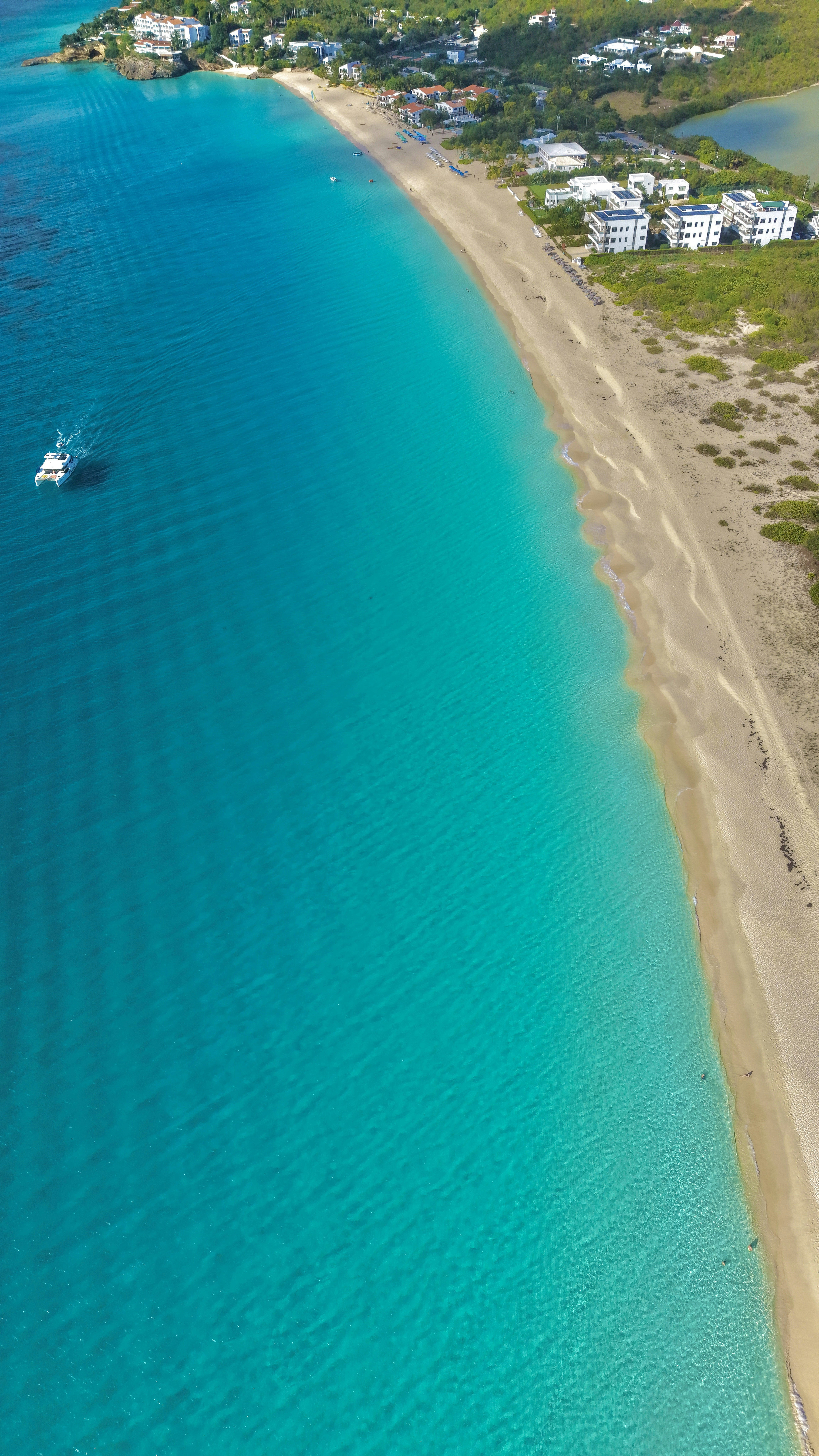 Tropical beach with turquoise water, boat, and coastal buildings.