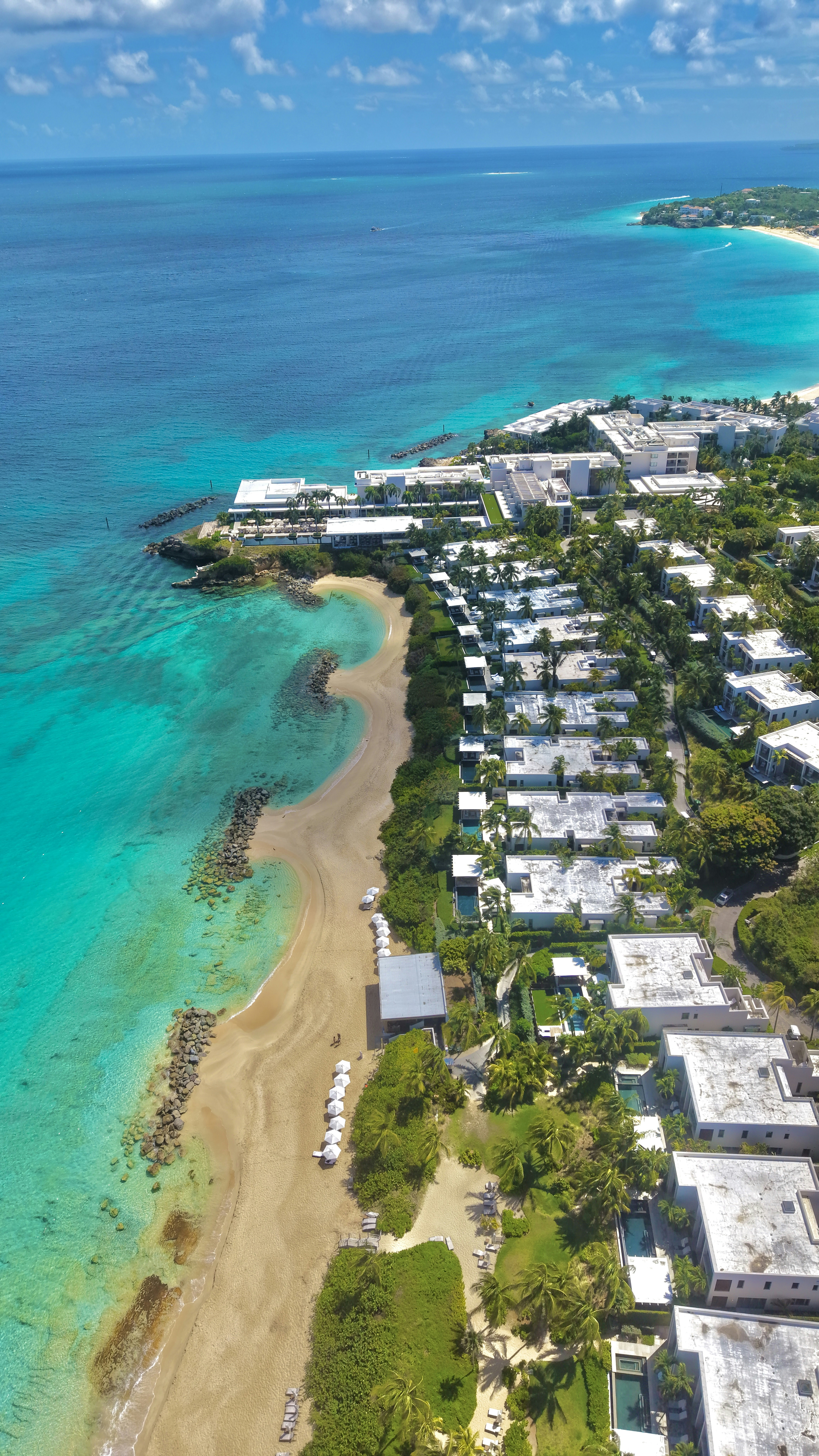 Tropical coastline with sandy beach, resort buildings, and turquoise ocean.