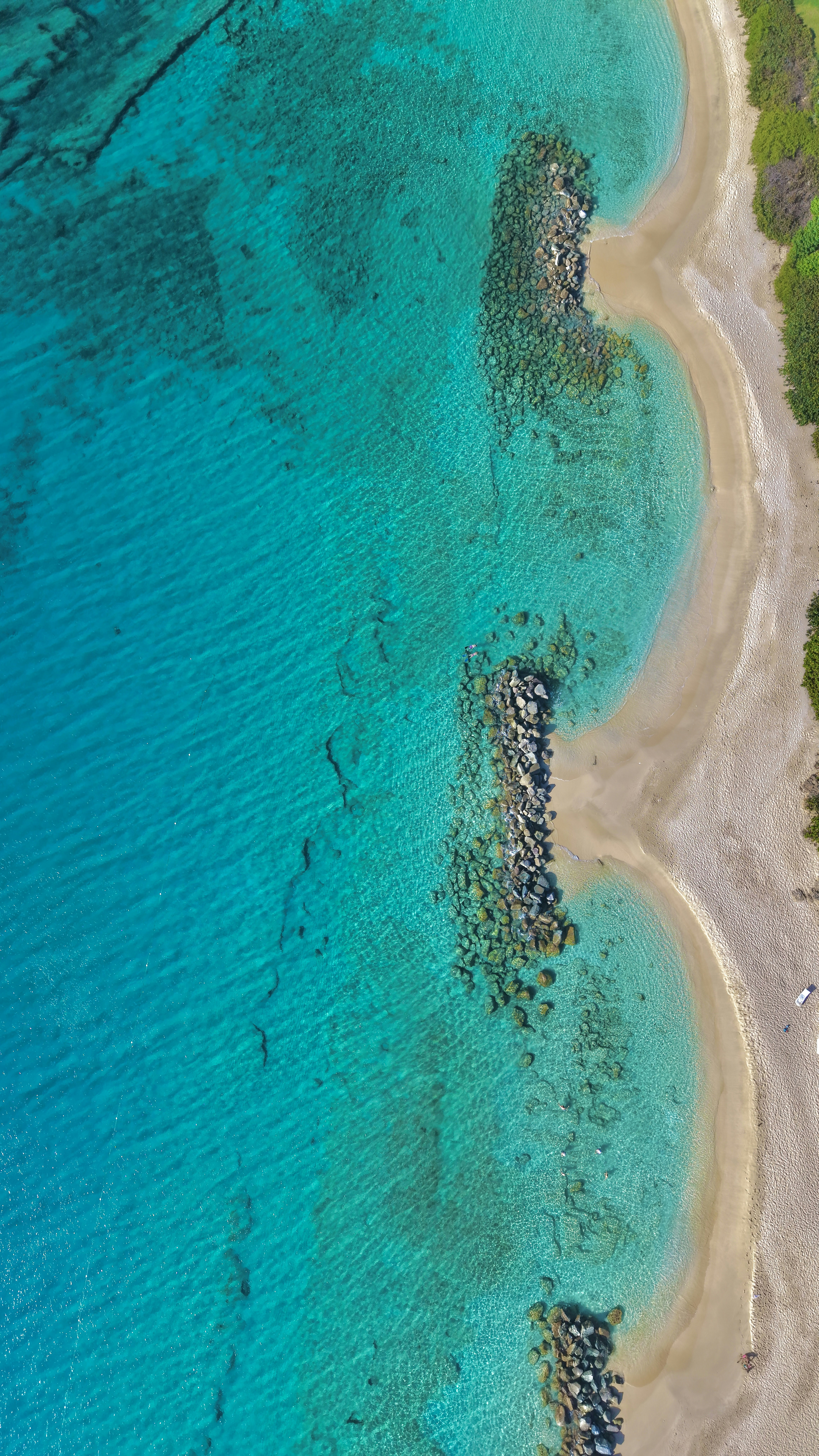 Turquoise ocean and sandy coves with rock jetties from above.