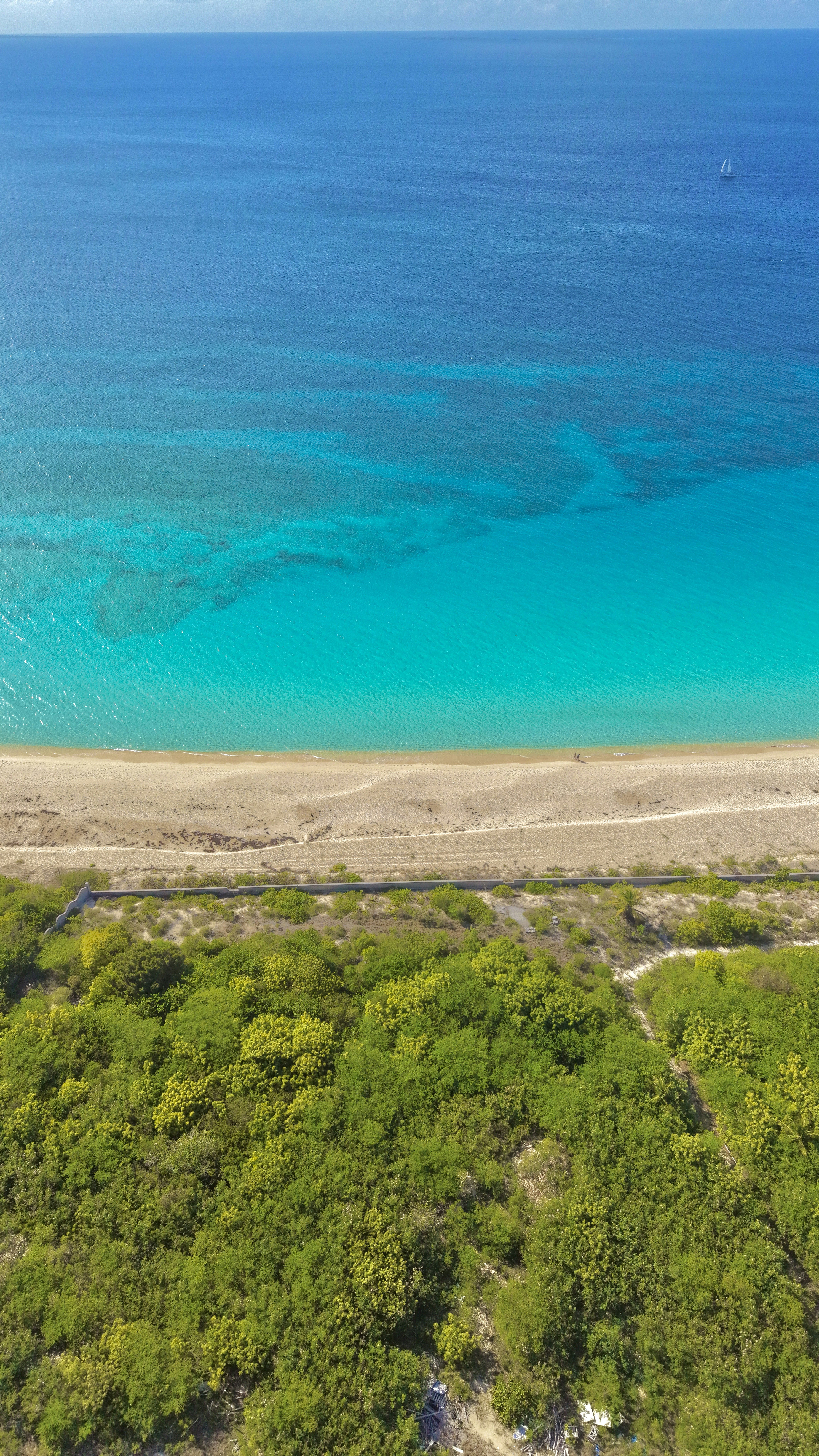 Aerial view of tropical beach, turquoise ocean, and green vegetation.