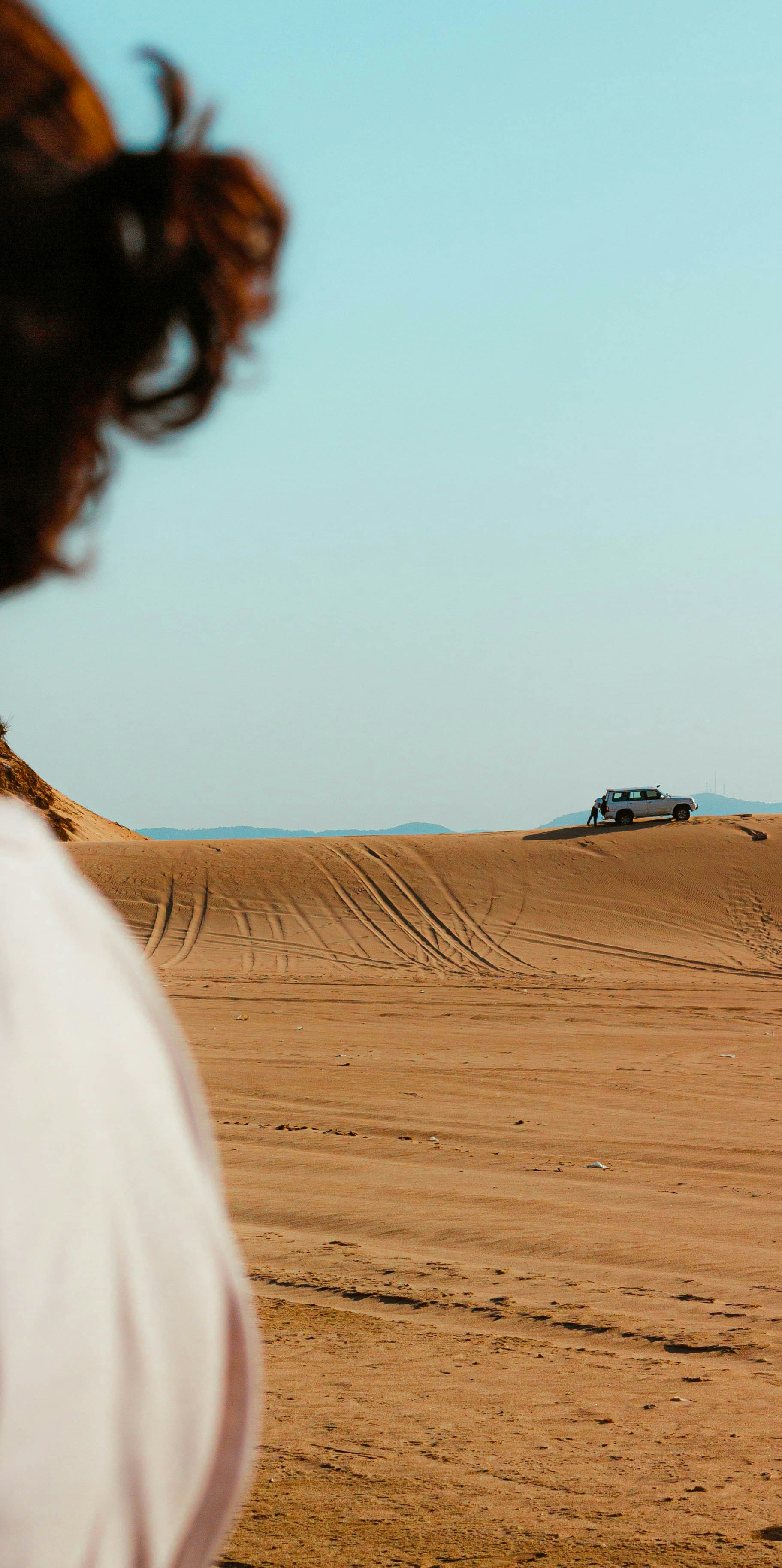 Person looks at truck on distant desert dune.