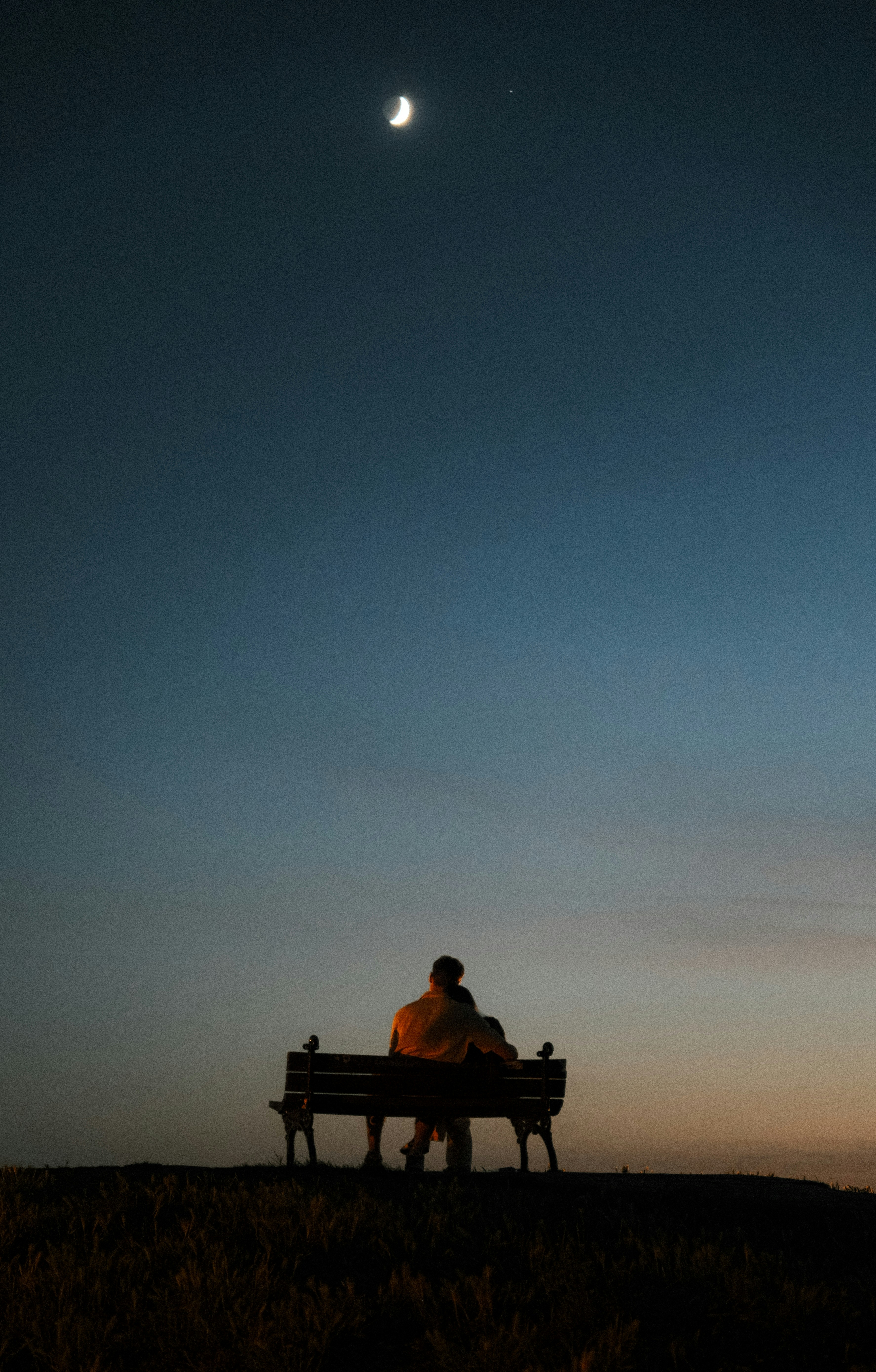 Couple on bench under a crescent moon