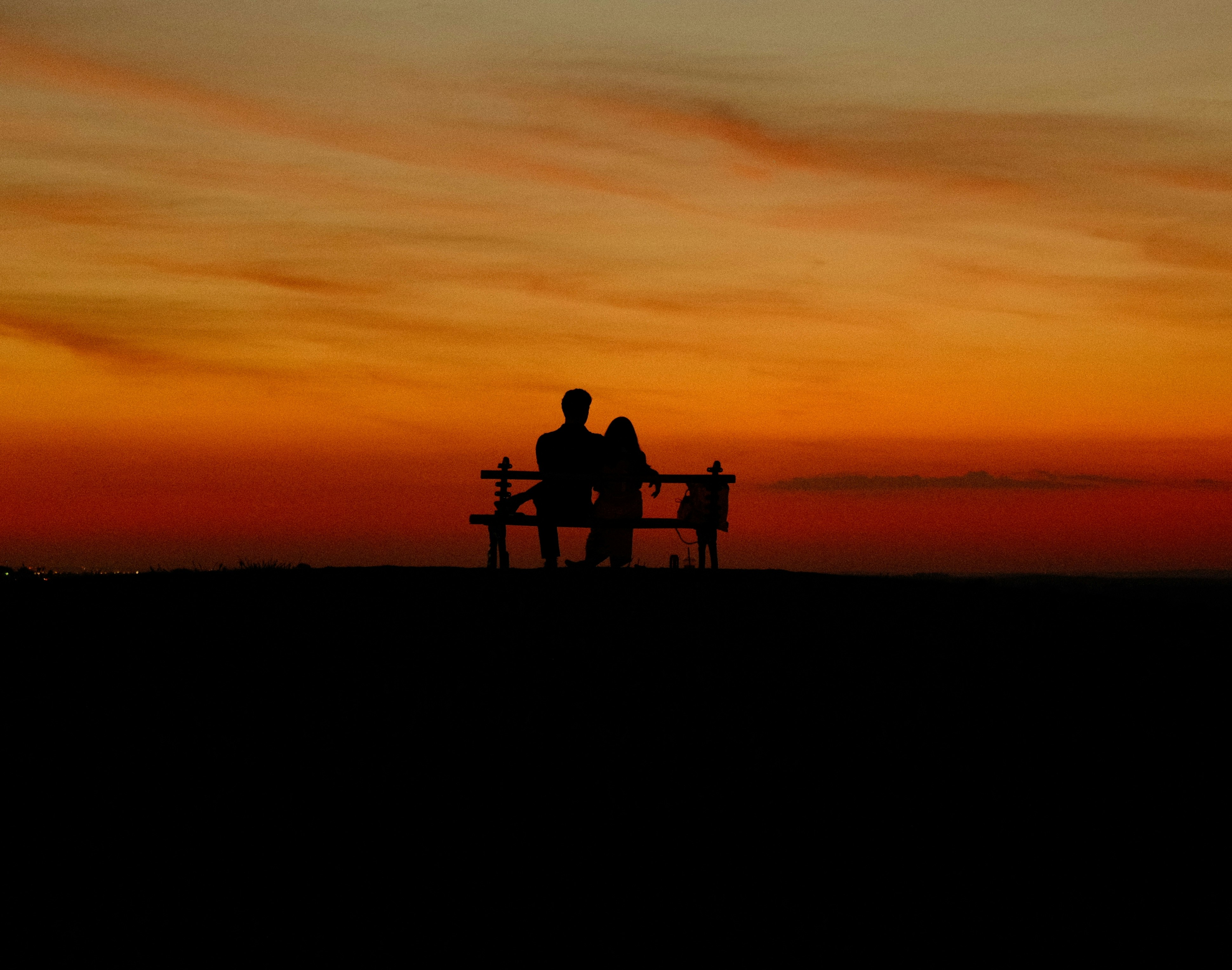 Two people silhouetted on a bench against a vibrant sunset