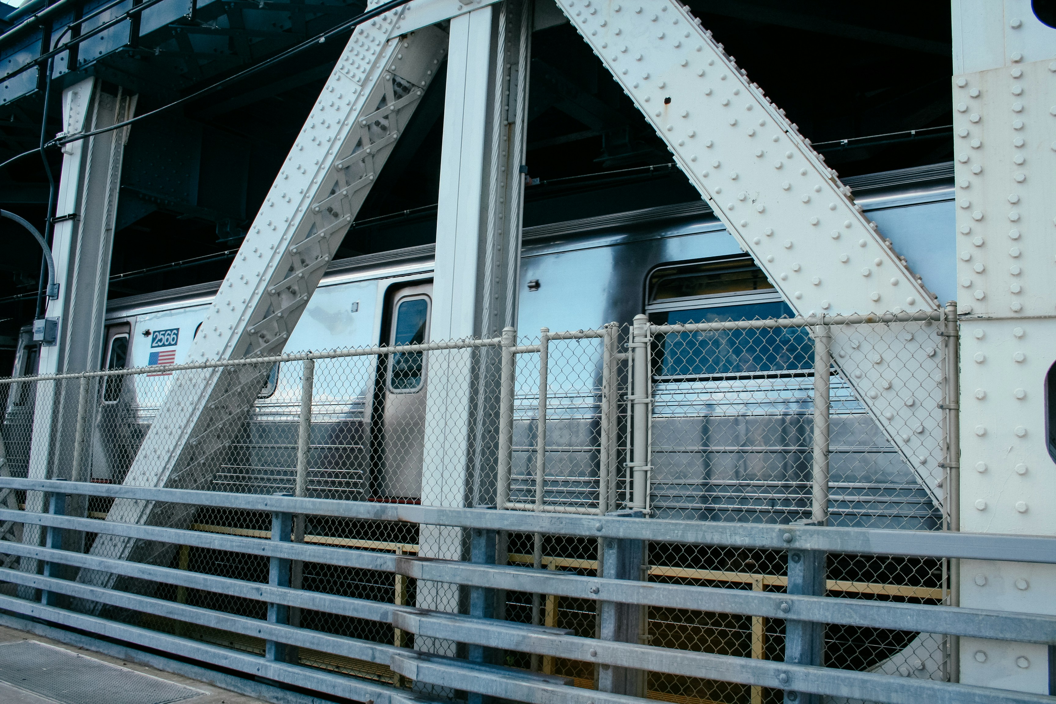 Silver train behind a steel bridge truss