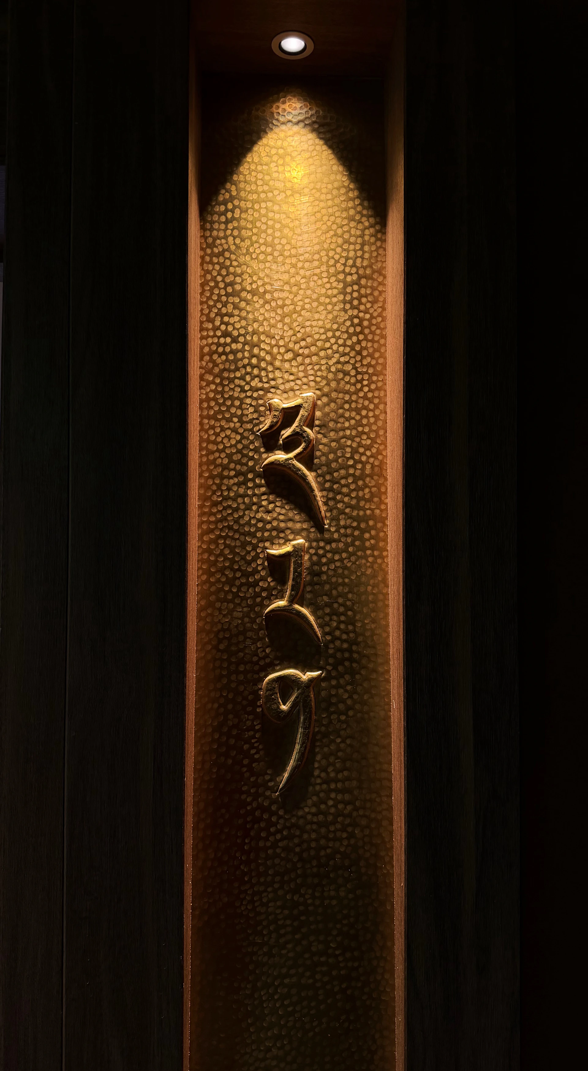 Gold Tibetan script on a hammered metal panel illuminated by a spotlight