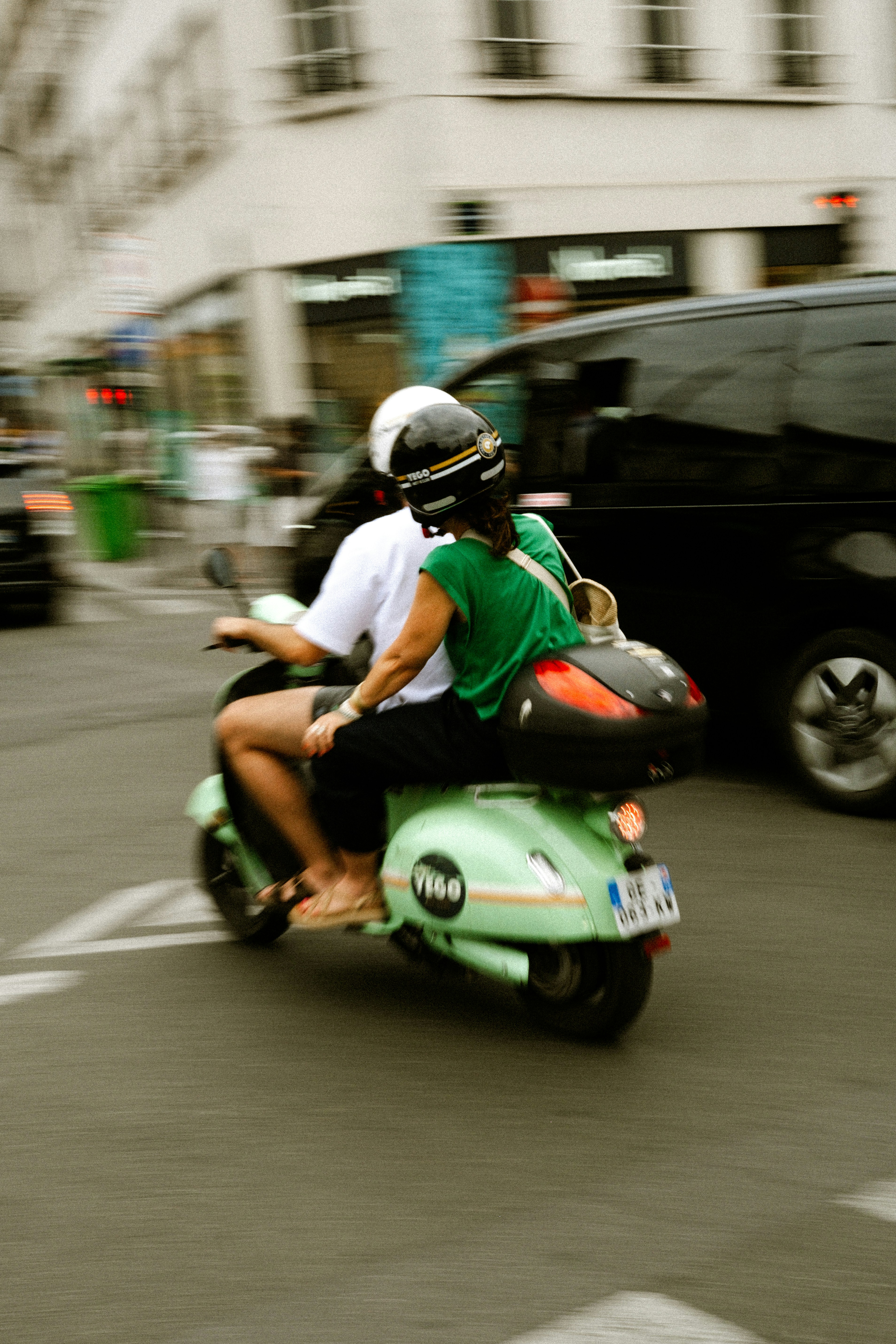 Two people ride a green scooter on a city street. - 相关推荐