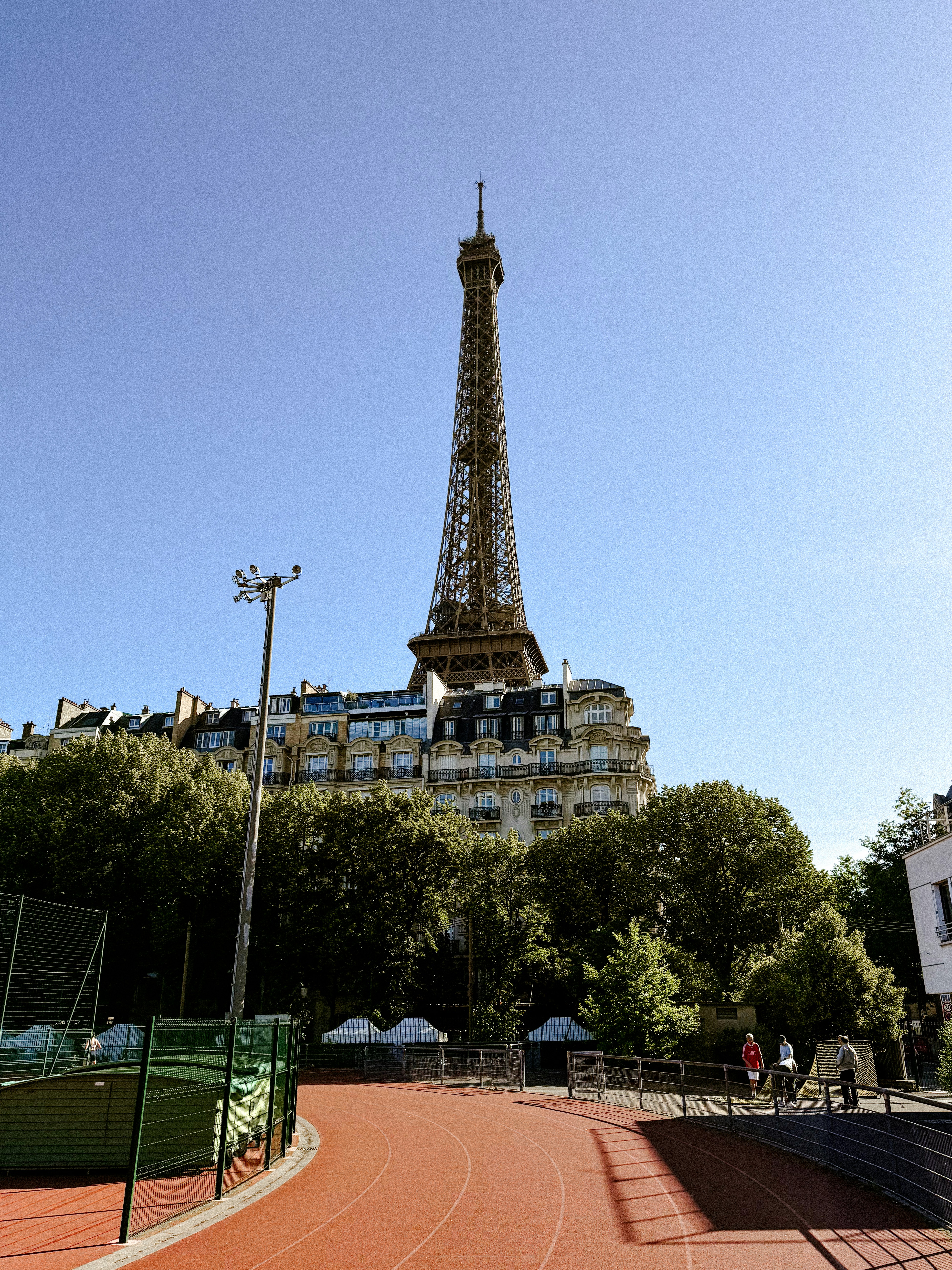 Eiffel tower overlooking buildings, trees, and a red running track.
