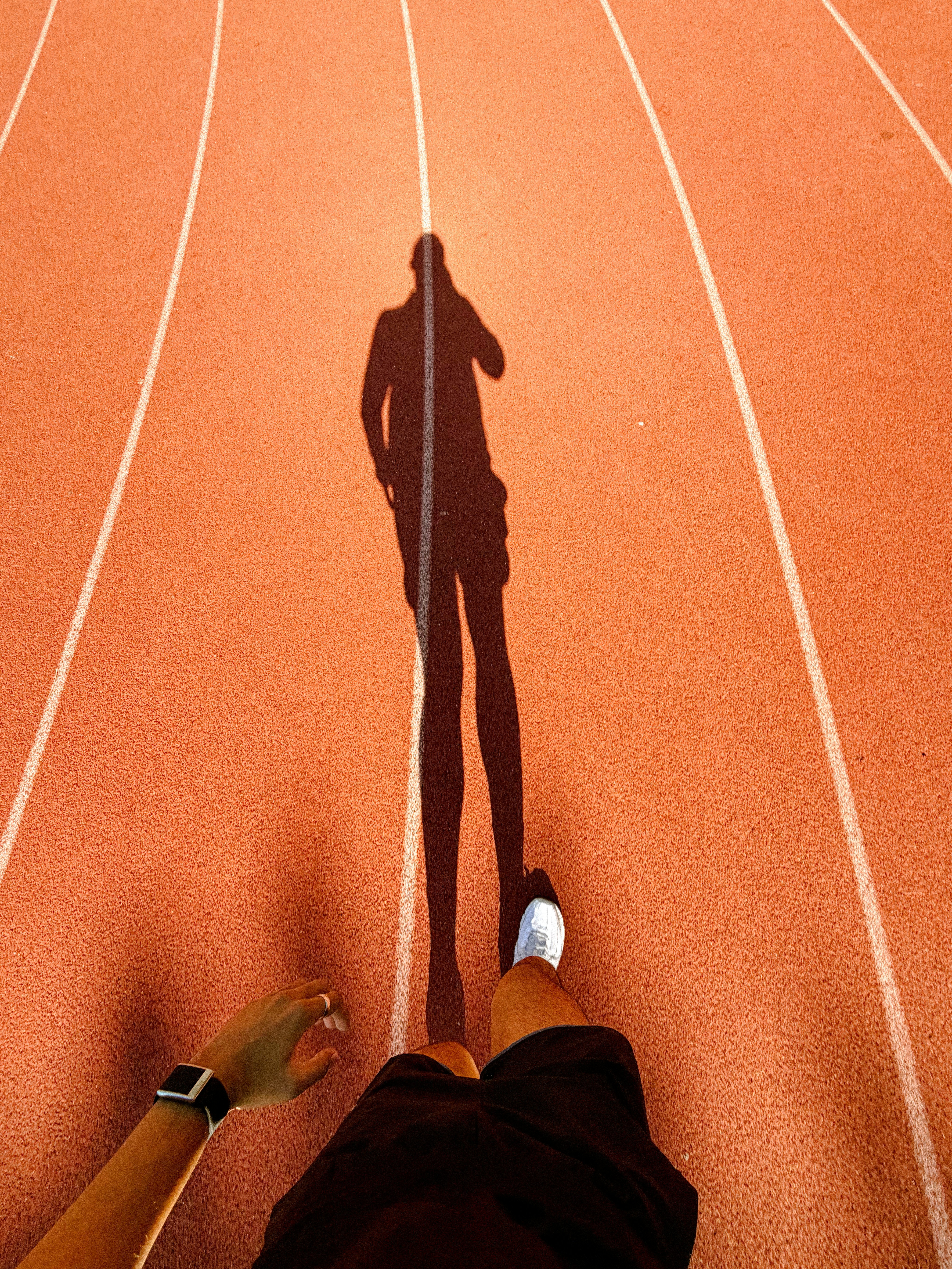 Runner's shadow stretching across an orange athletic track.