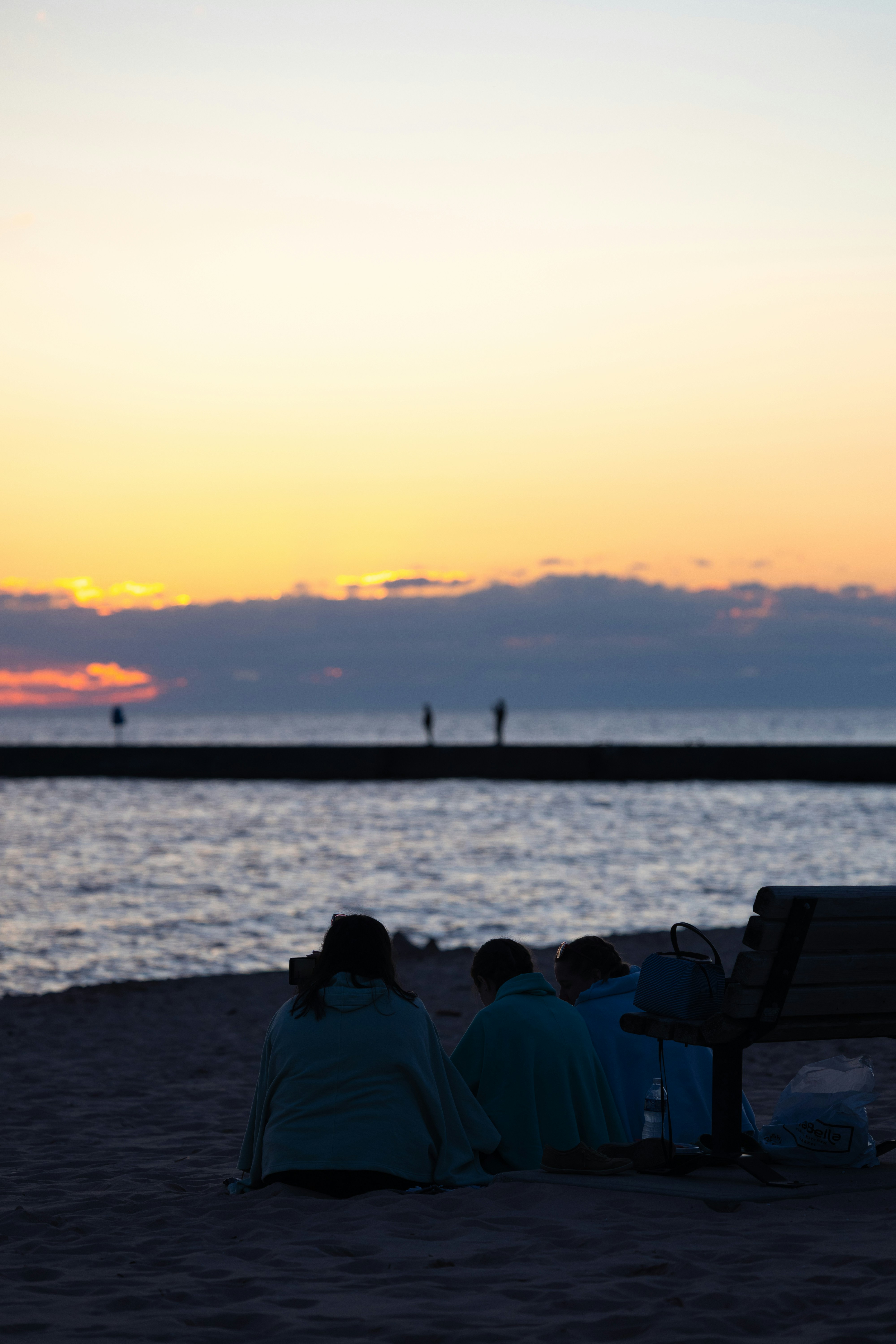 Figuras en silueta en una playa al atardecer cerca de un muelle