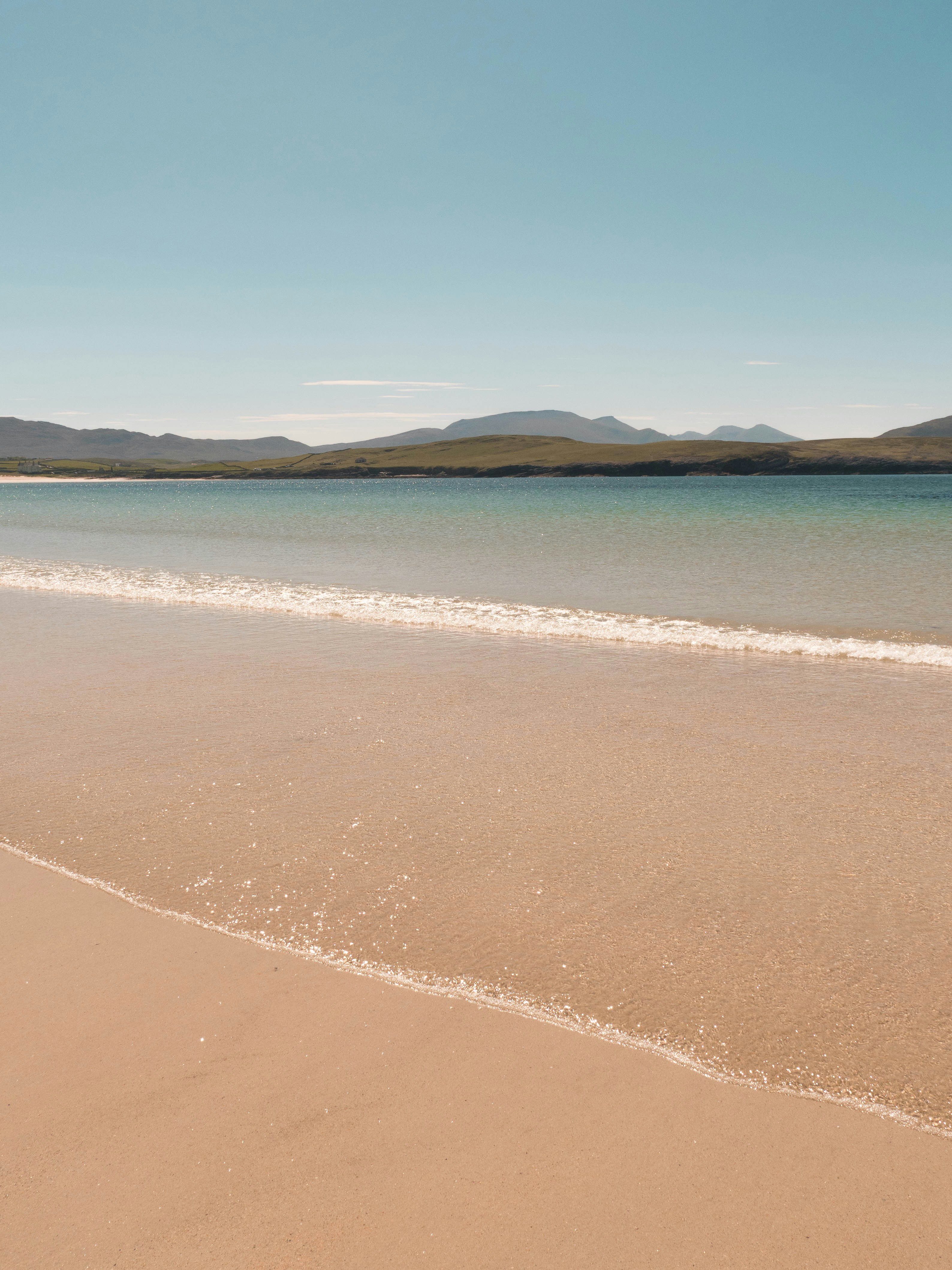 Serene sandy beach with clear water and distant mountains