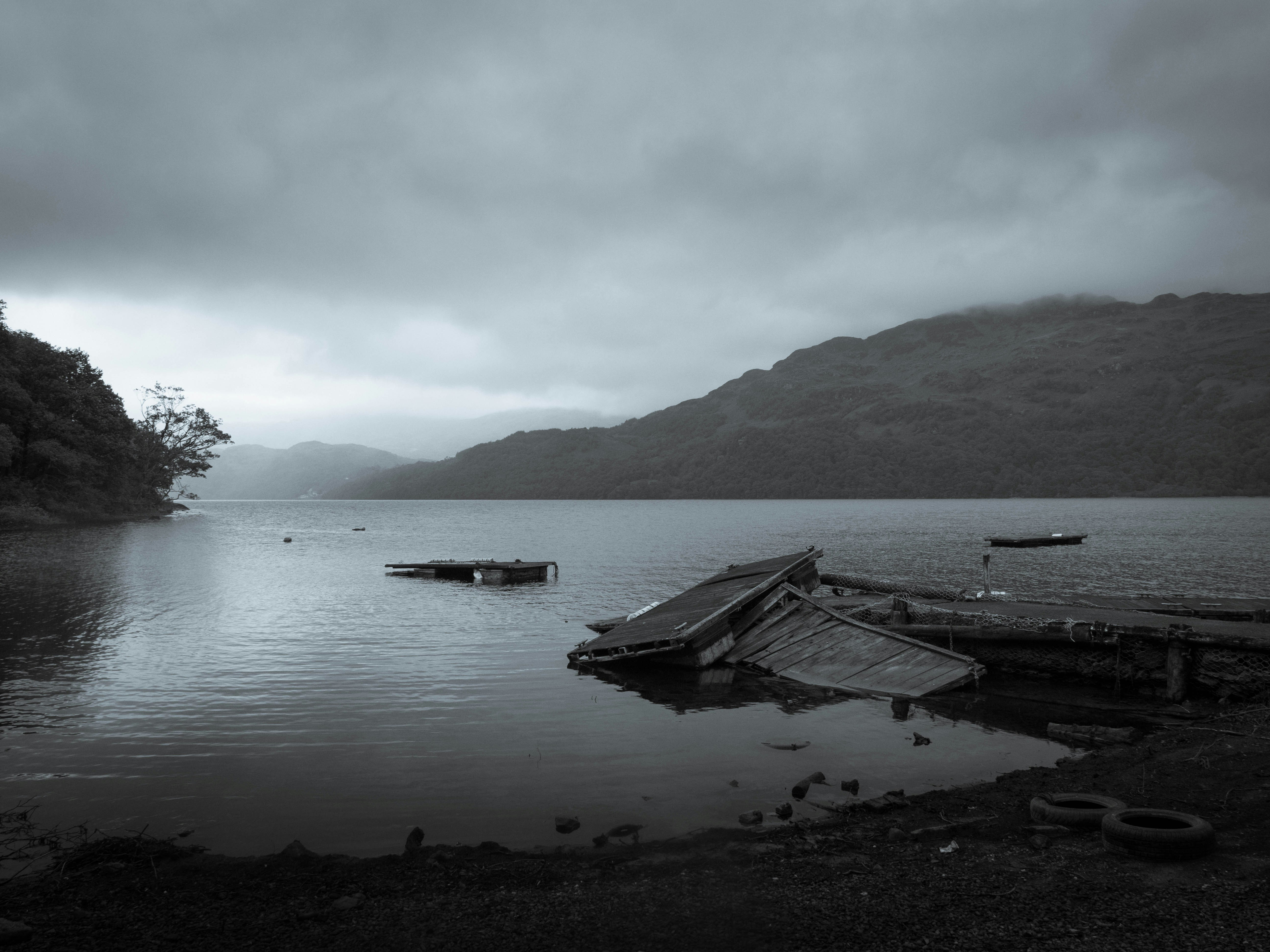 Gloomy lake scene with mountains and sunken debris