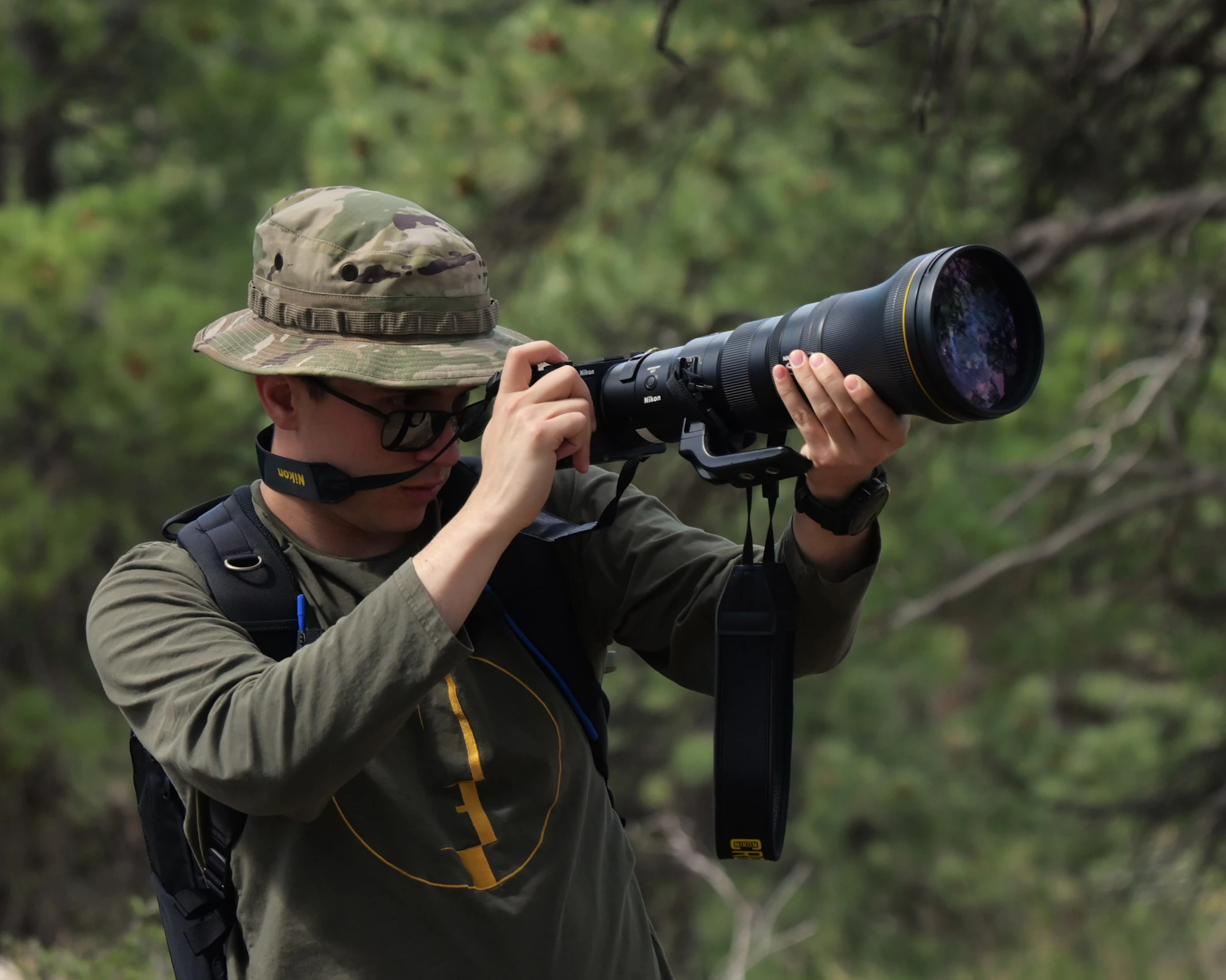 A photographer in a camouflage hat sighting down a long telephoto lens outdoors