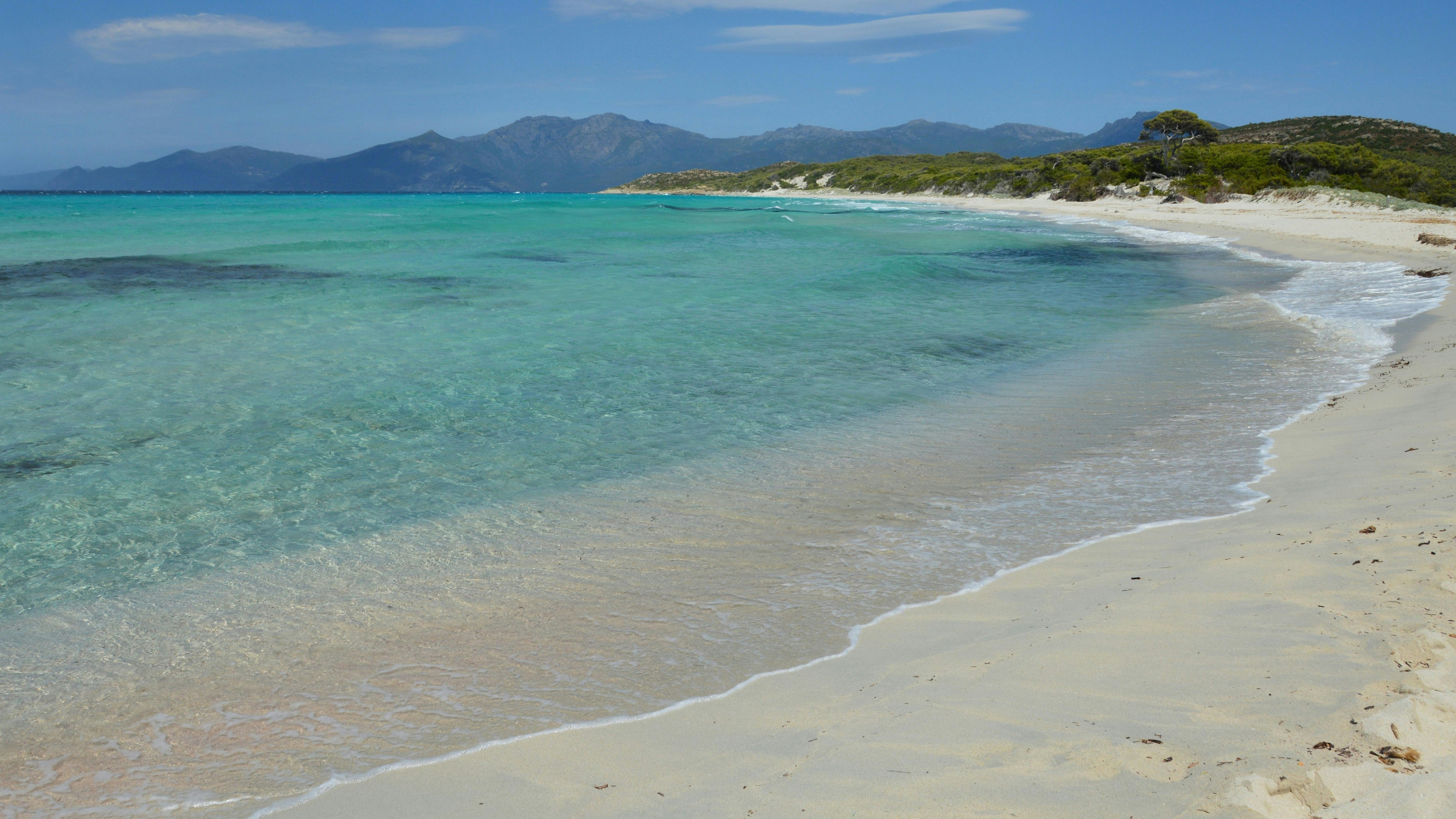 Plage de sable blanc avec une eau turquoise claire et montagnes lointaines.