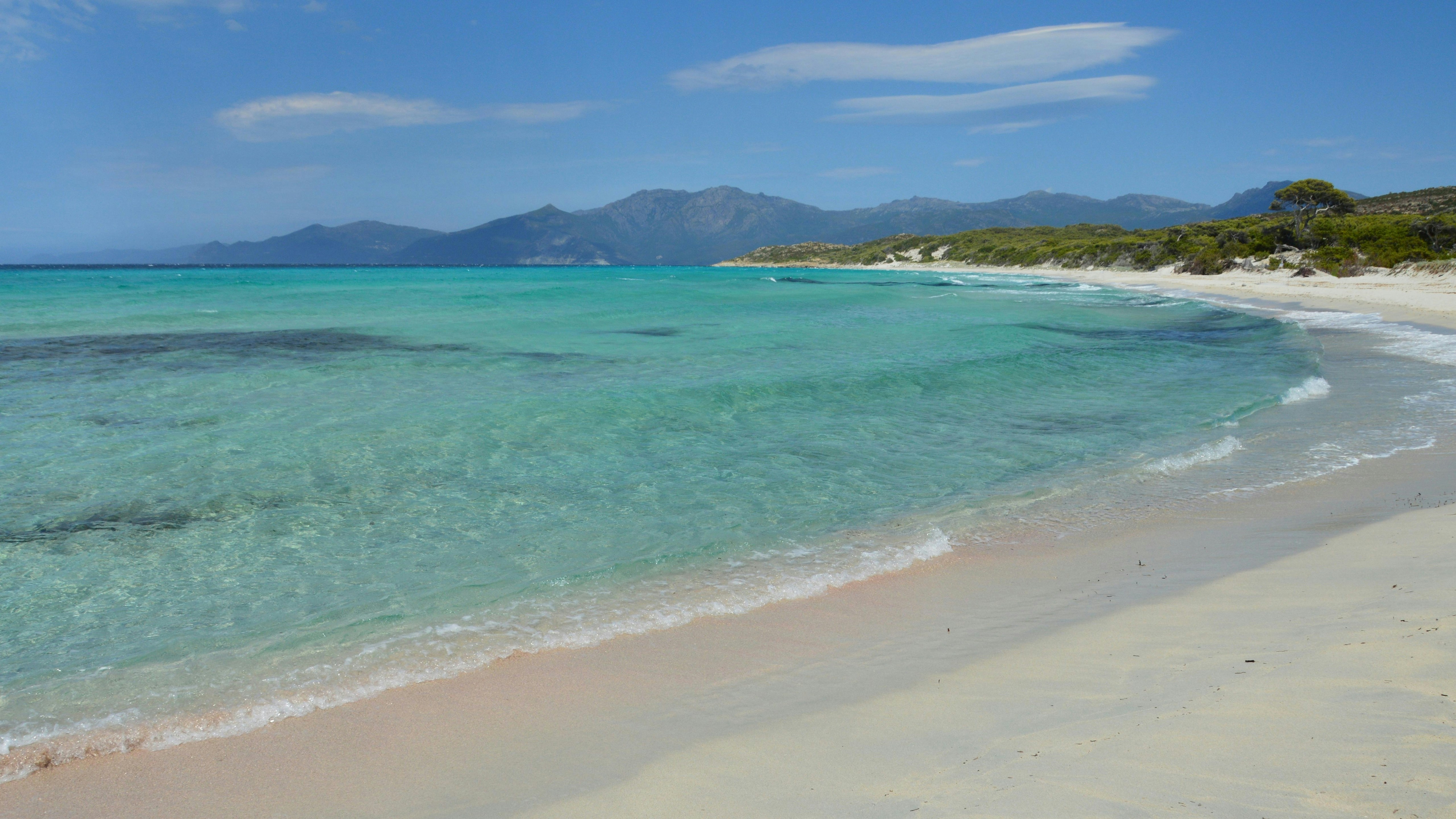 Eau turquoise claire et plage de sable blanc avec des montagnes lointaines.