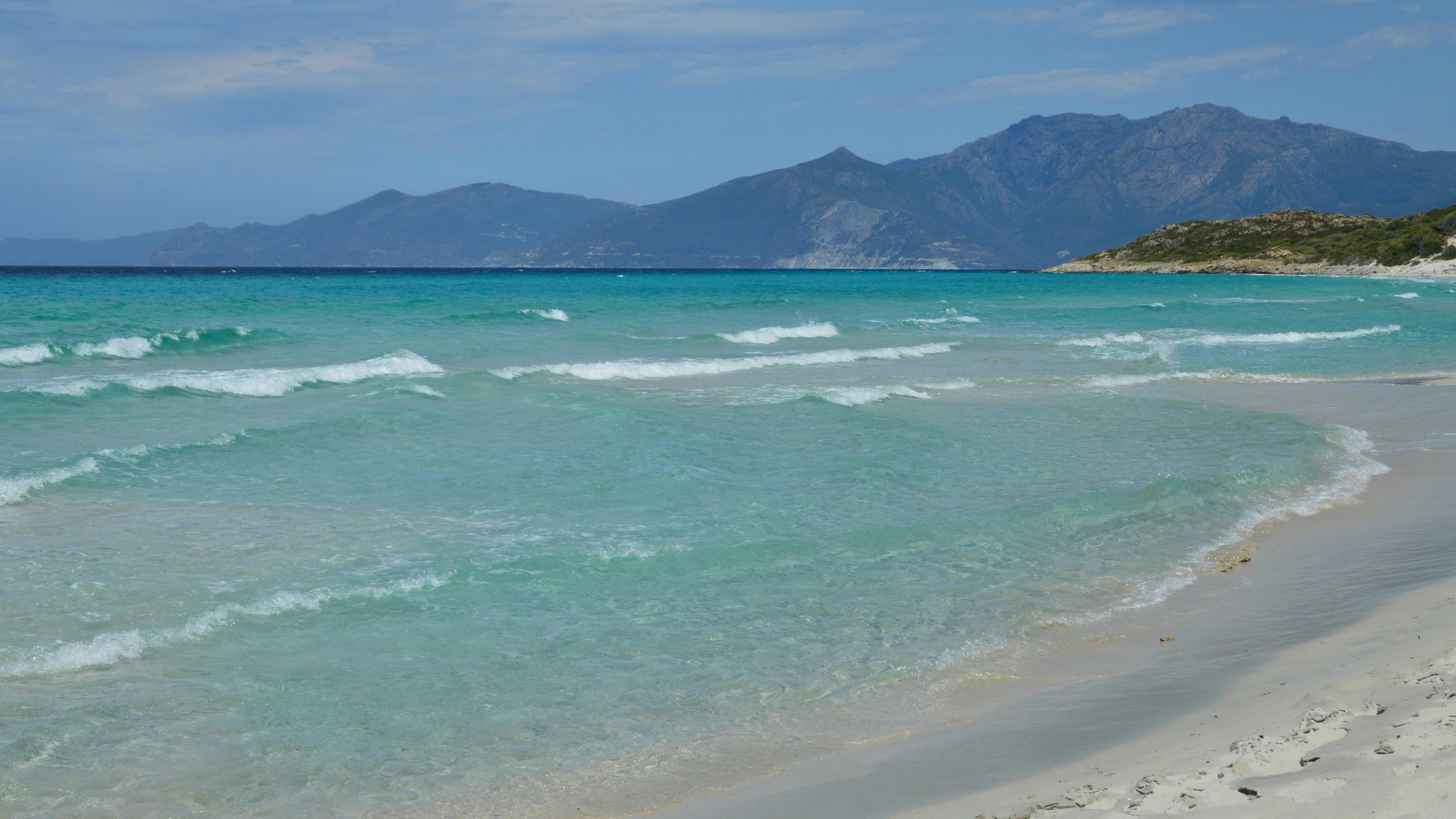 Clear turquoise ocean waves on a sandy beach with mountains.