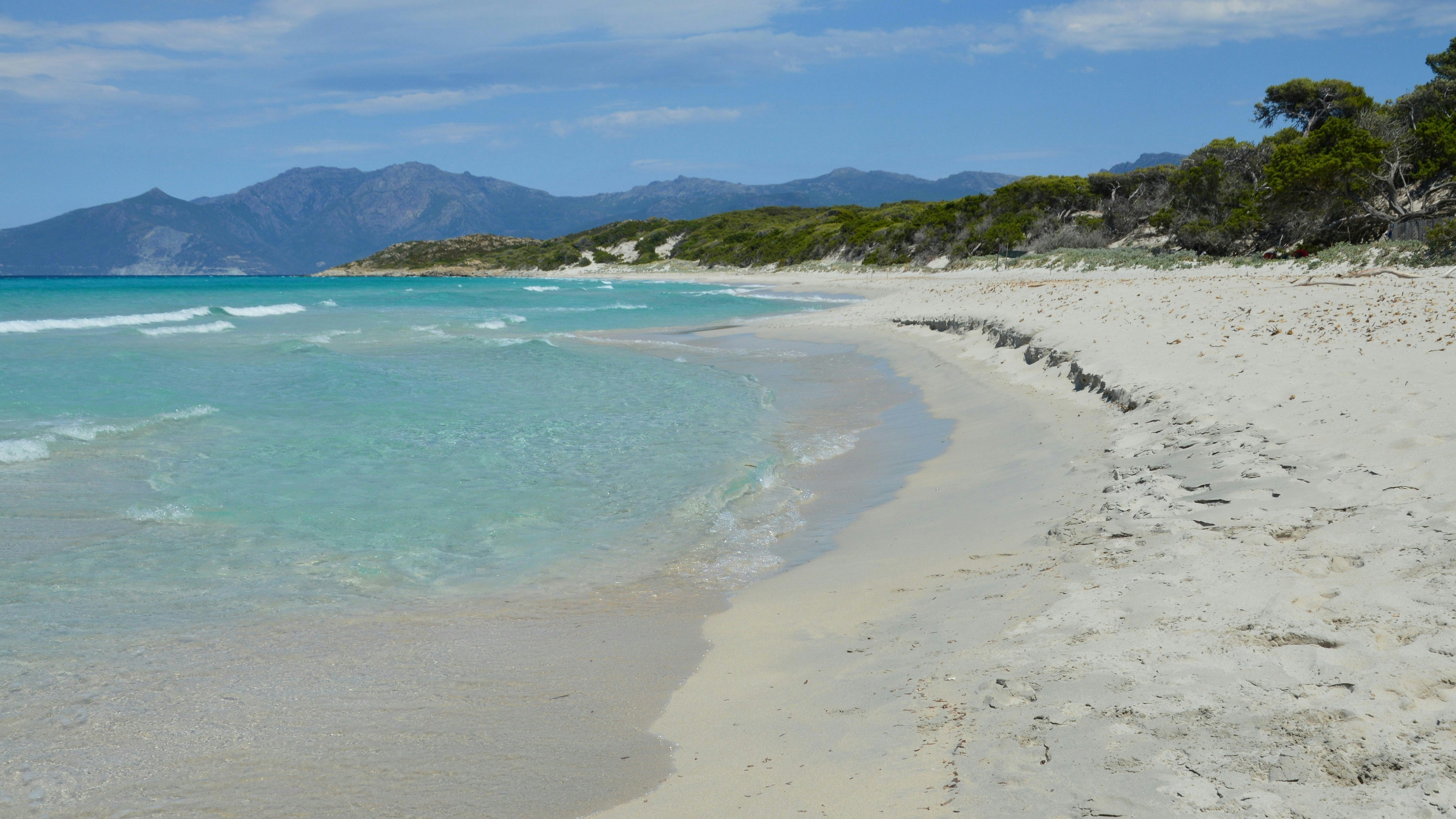 Plage de sable blanc avec une eau turquoise claire et montagnes lointaines.