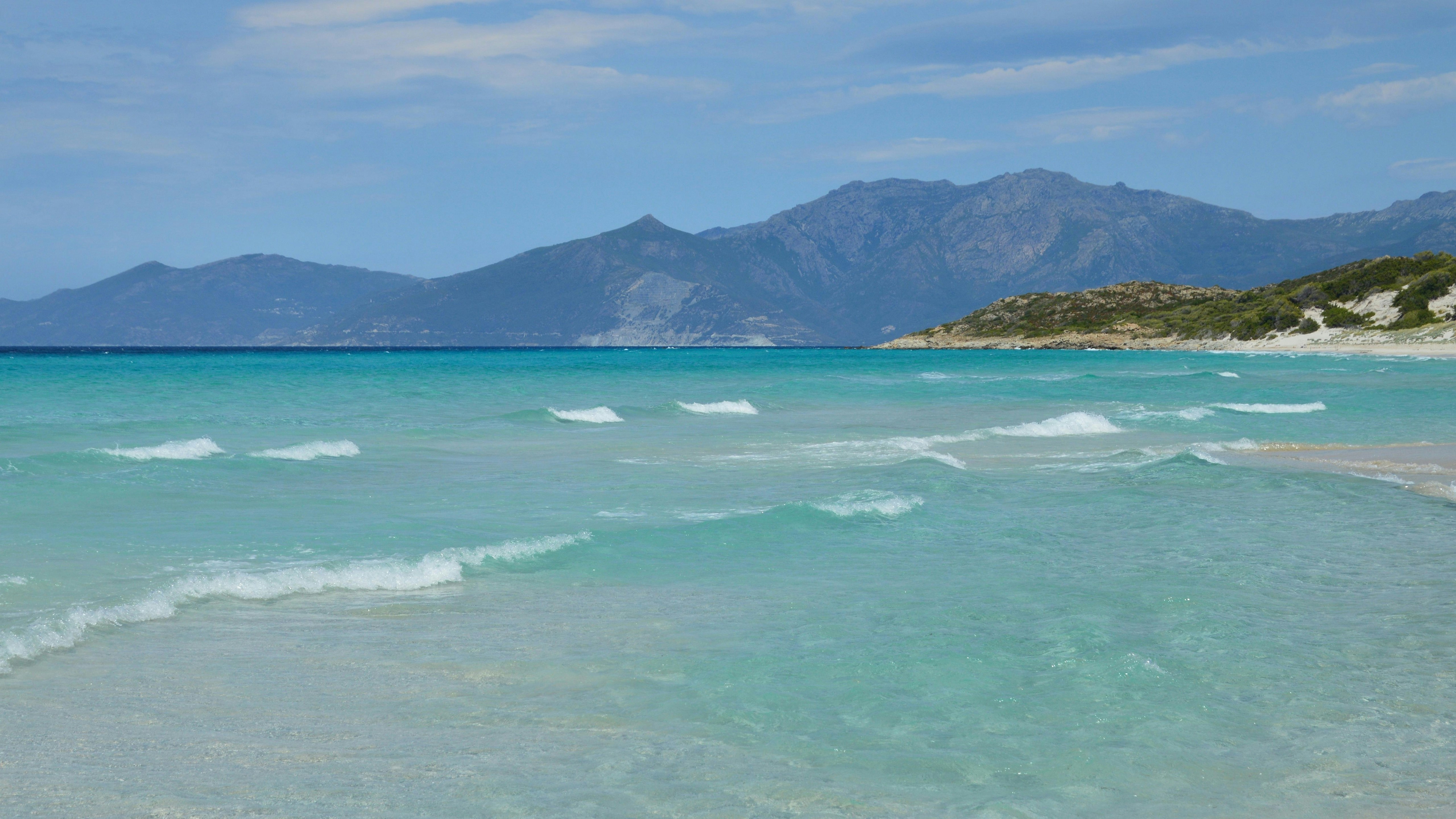 Des vagues turquoise claires sur une plage de sable avec des montagnes.