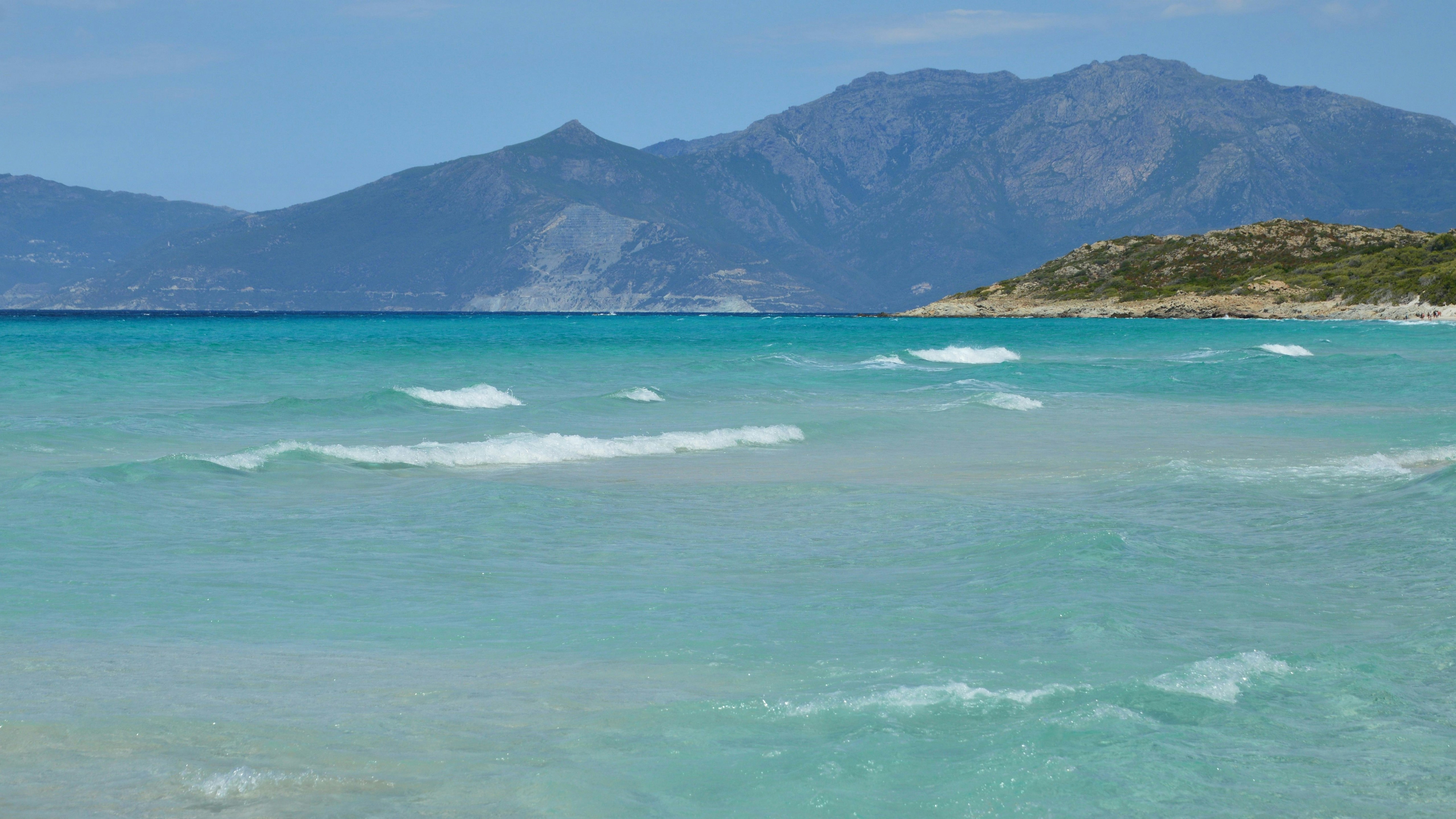 Des vagues turquoise de l’océan avec des montagnes lointaines et un ciel bleu.