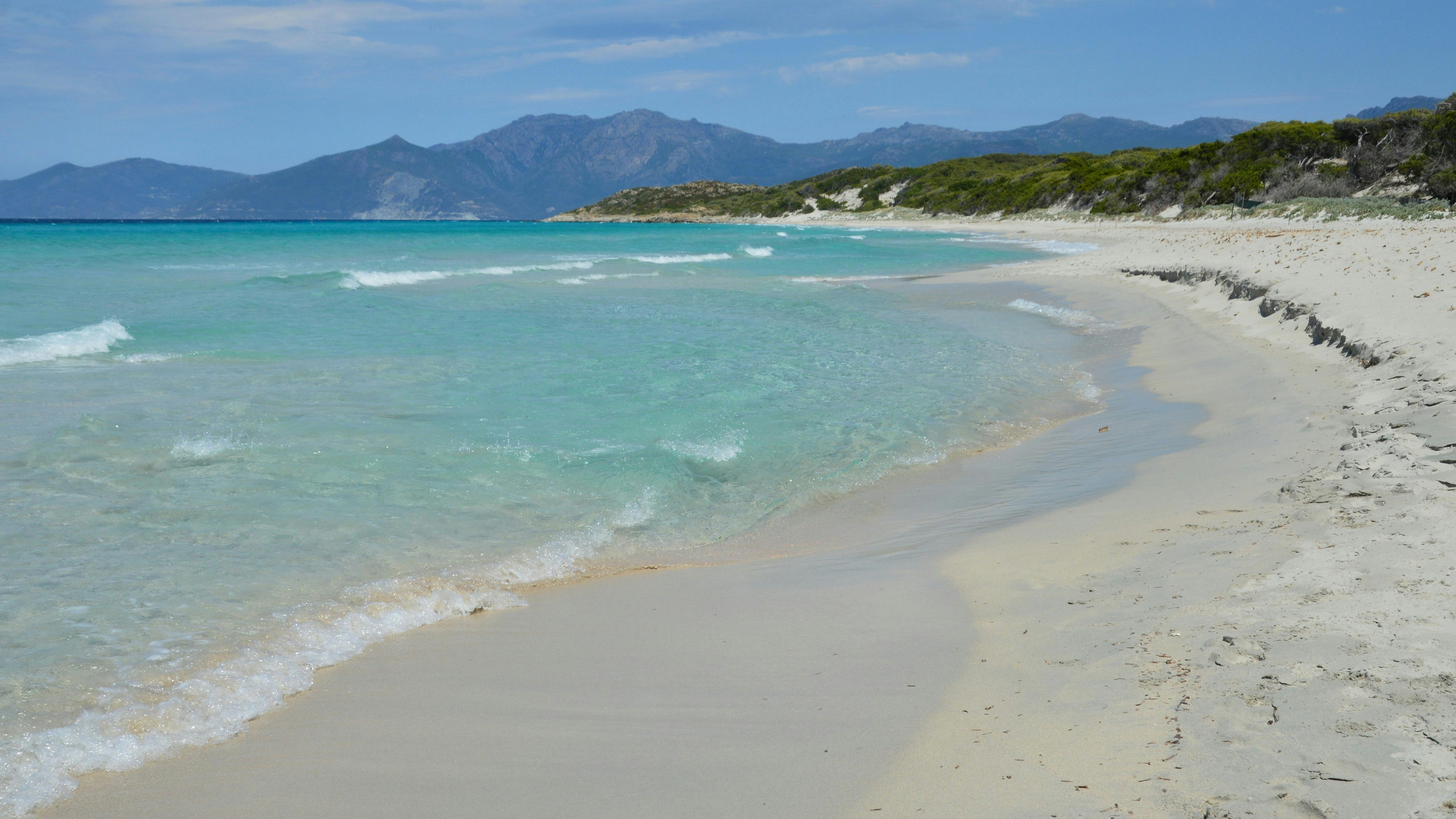 Belle plage de sable avec une eau turquoise claire et des montagnes lointaines.
