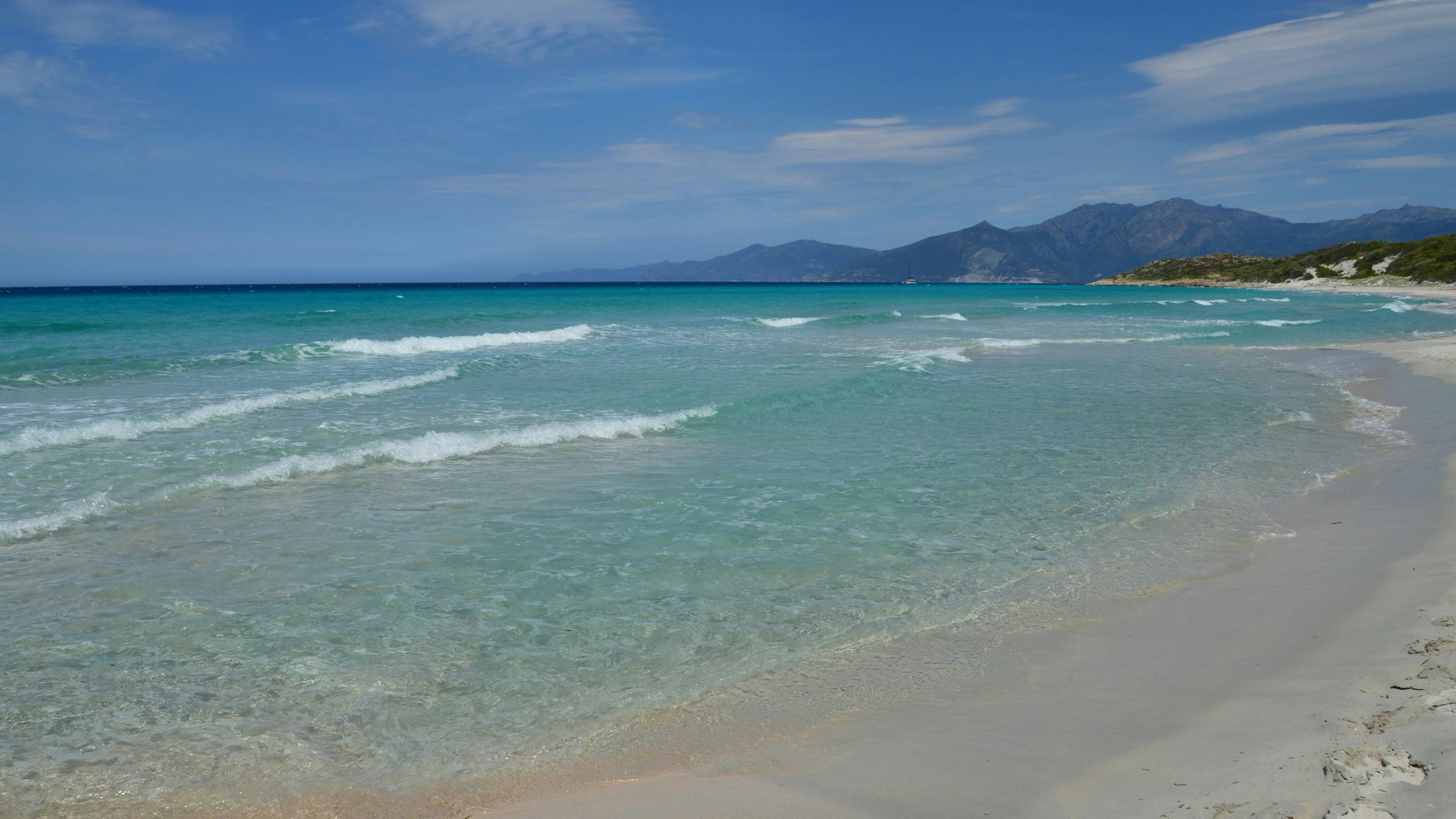 Plage de sable blanc, océan turquoise clair, et montagnes lointaines.