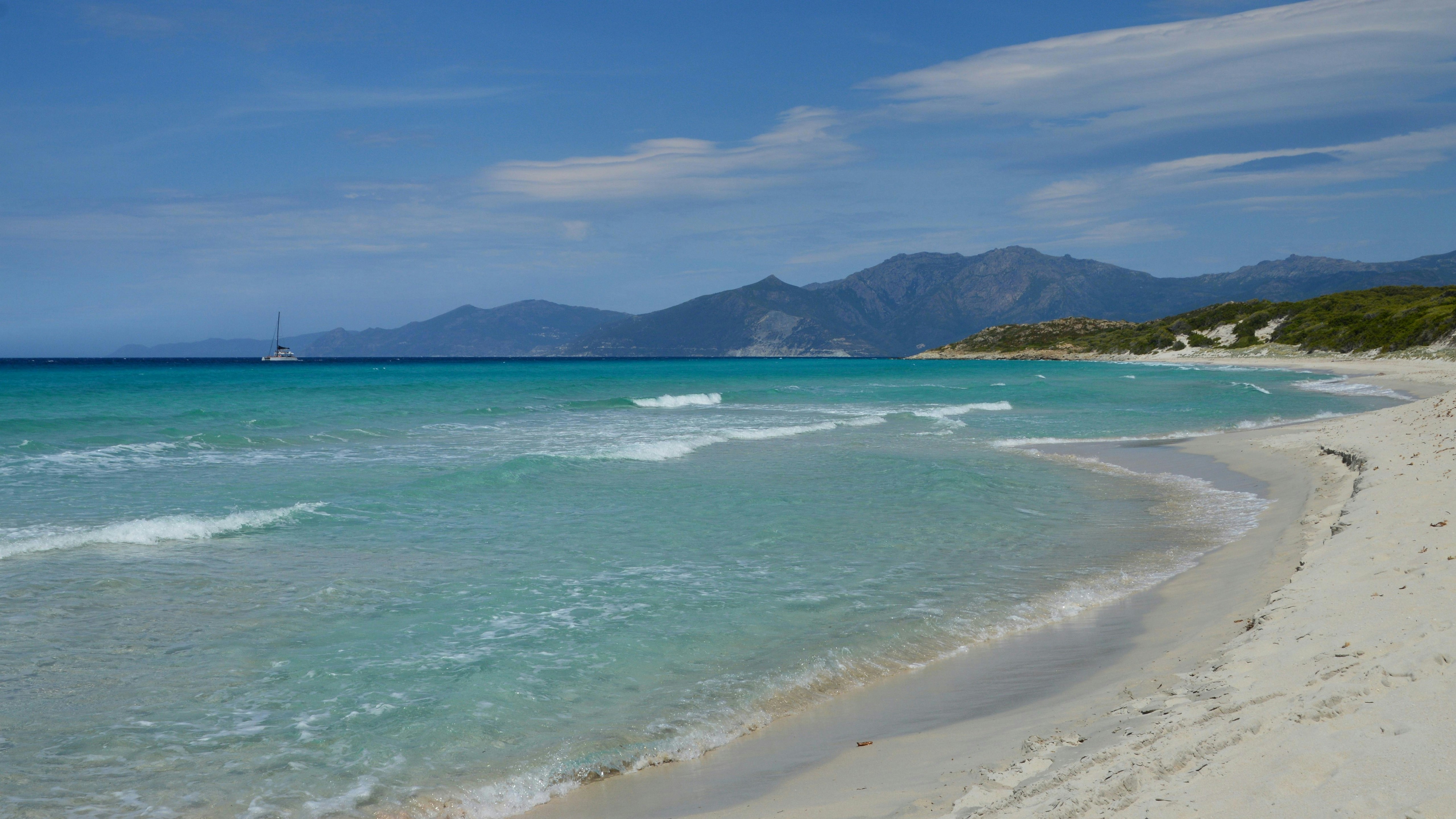 Plage de sable blanc avec une eau turquoise claire et montagnes lointaines.