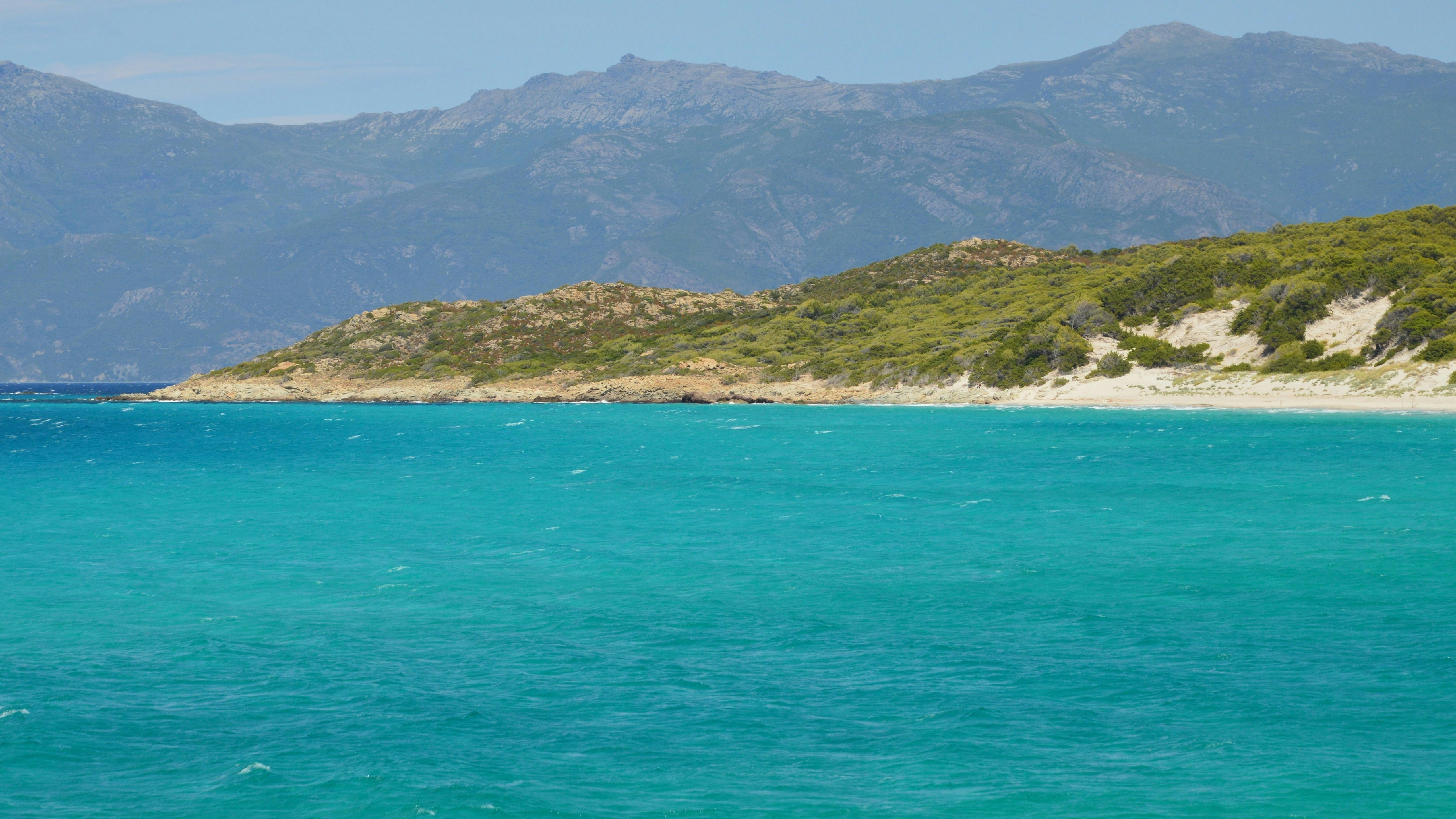 L’océan turquoise rencontre une côte verte avec des montagnes lointaines.