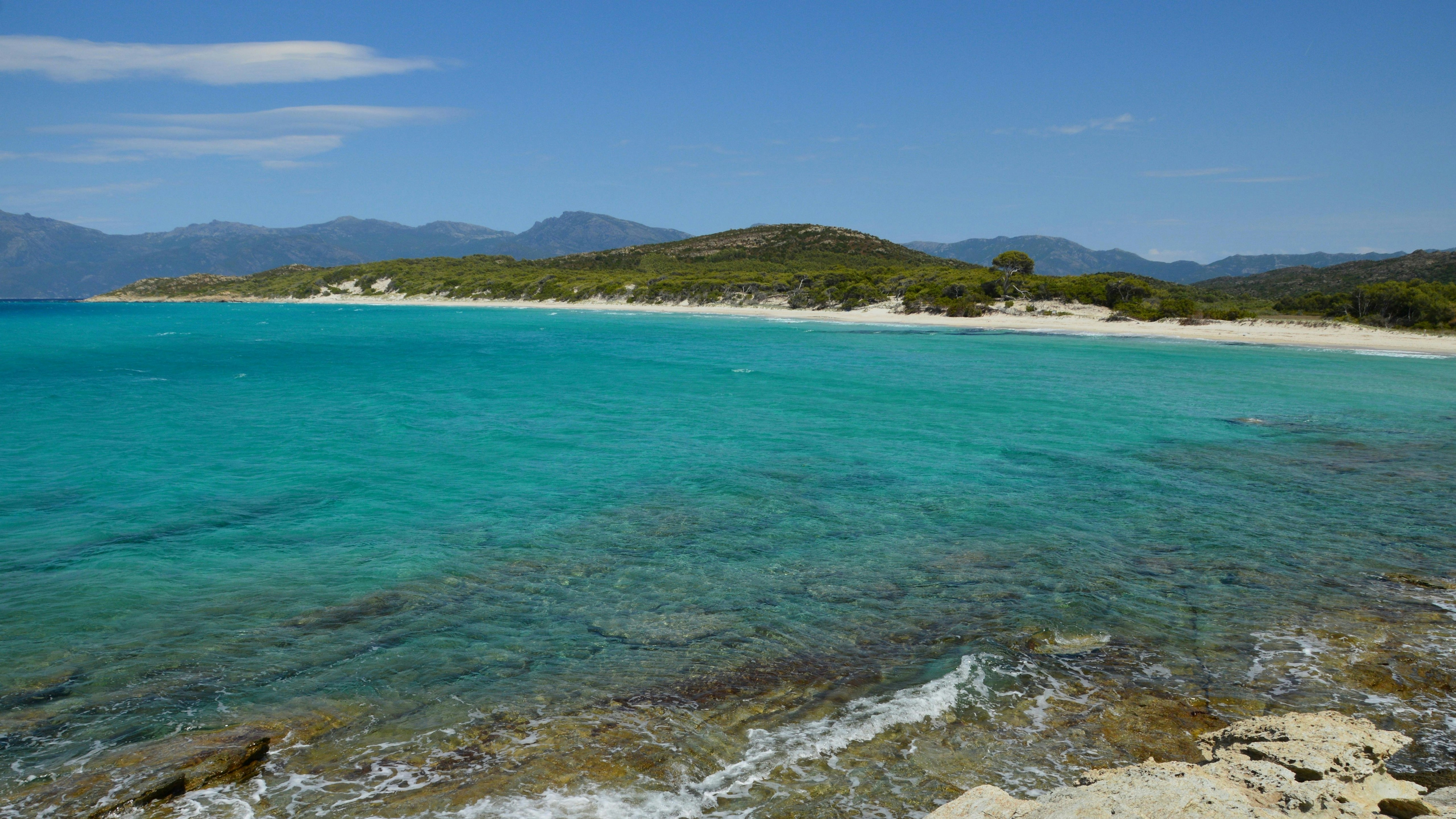 Une mer turquoise claire rencontre une plage de sable et des collines verdoyantes.