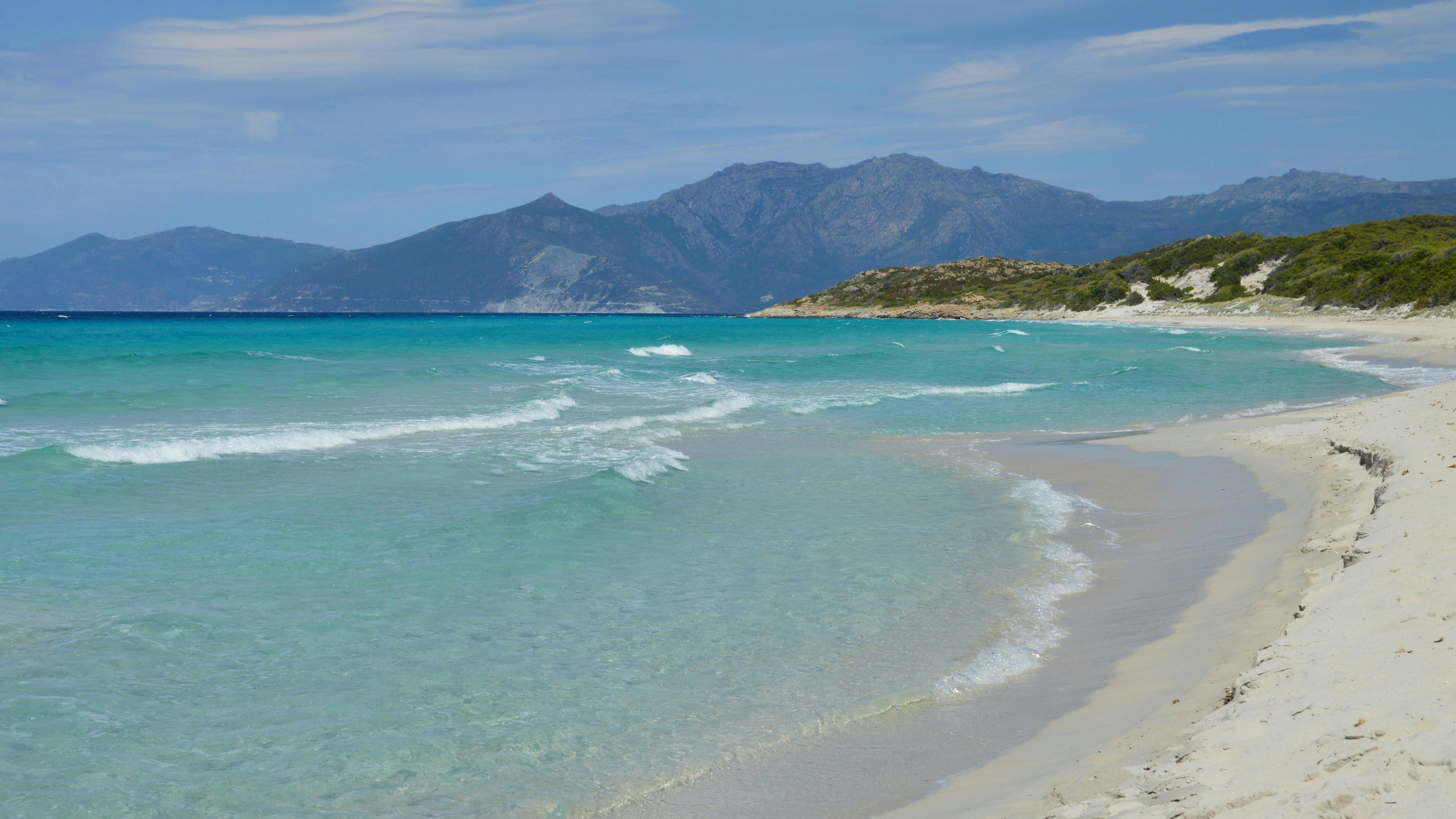 Magnifique océan turquoise, plage de sable blanc et montagnes lointaines.