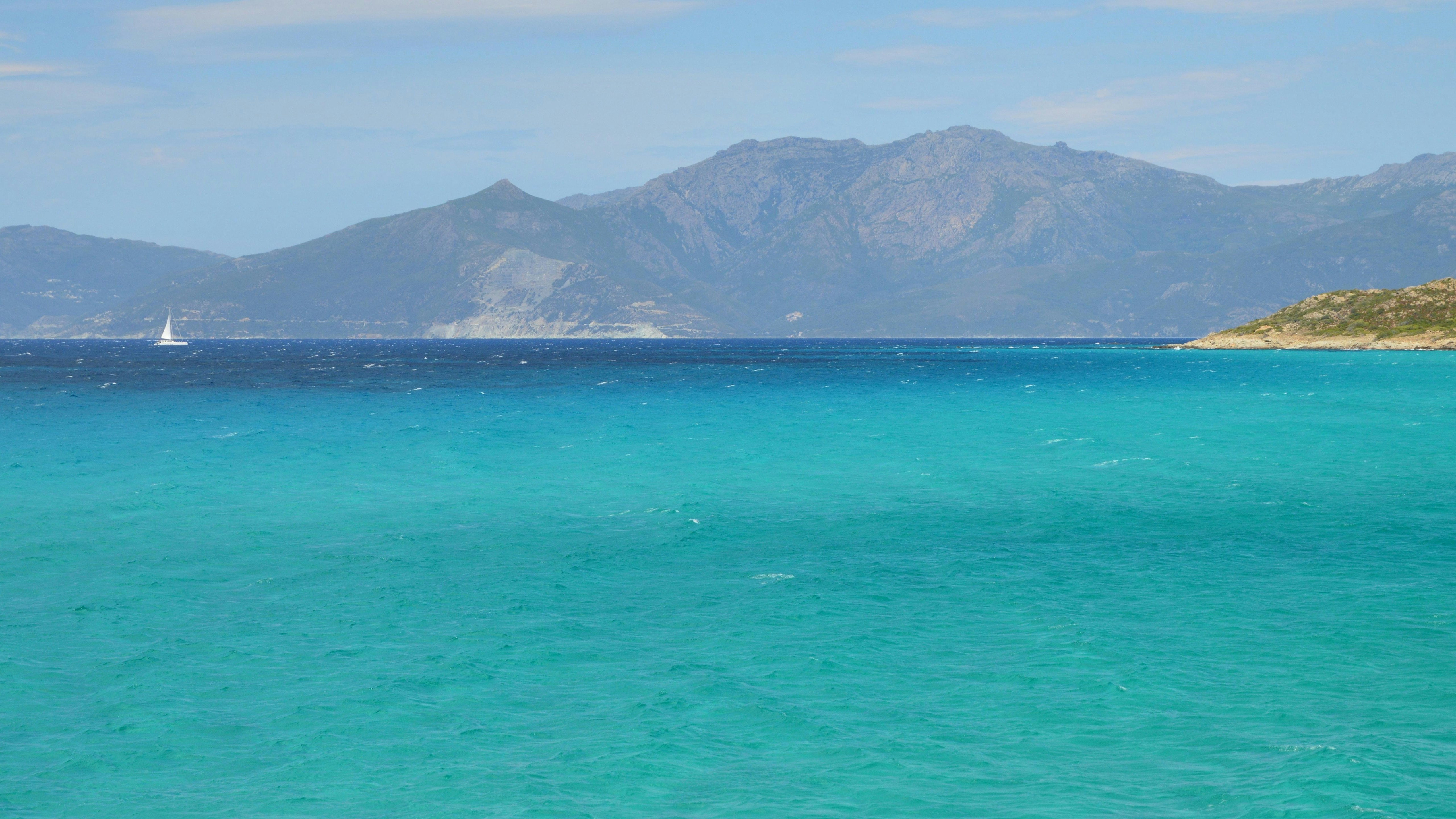 Océan turquoise avec des montagnes lointaines et un voilier.