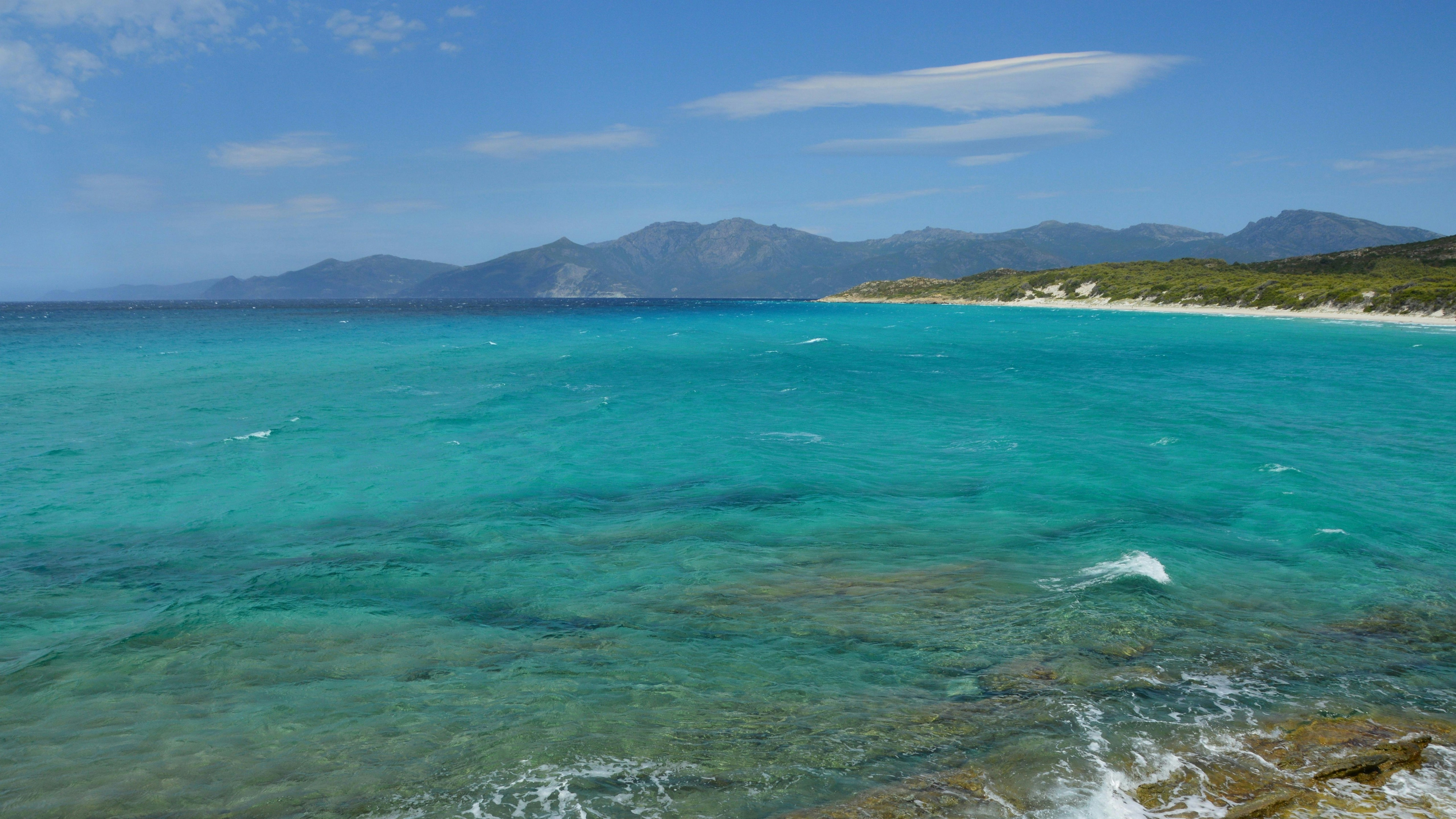 Océan turquoise avec une plage de sable et des montagnes lointaines.