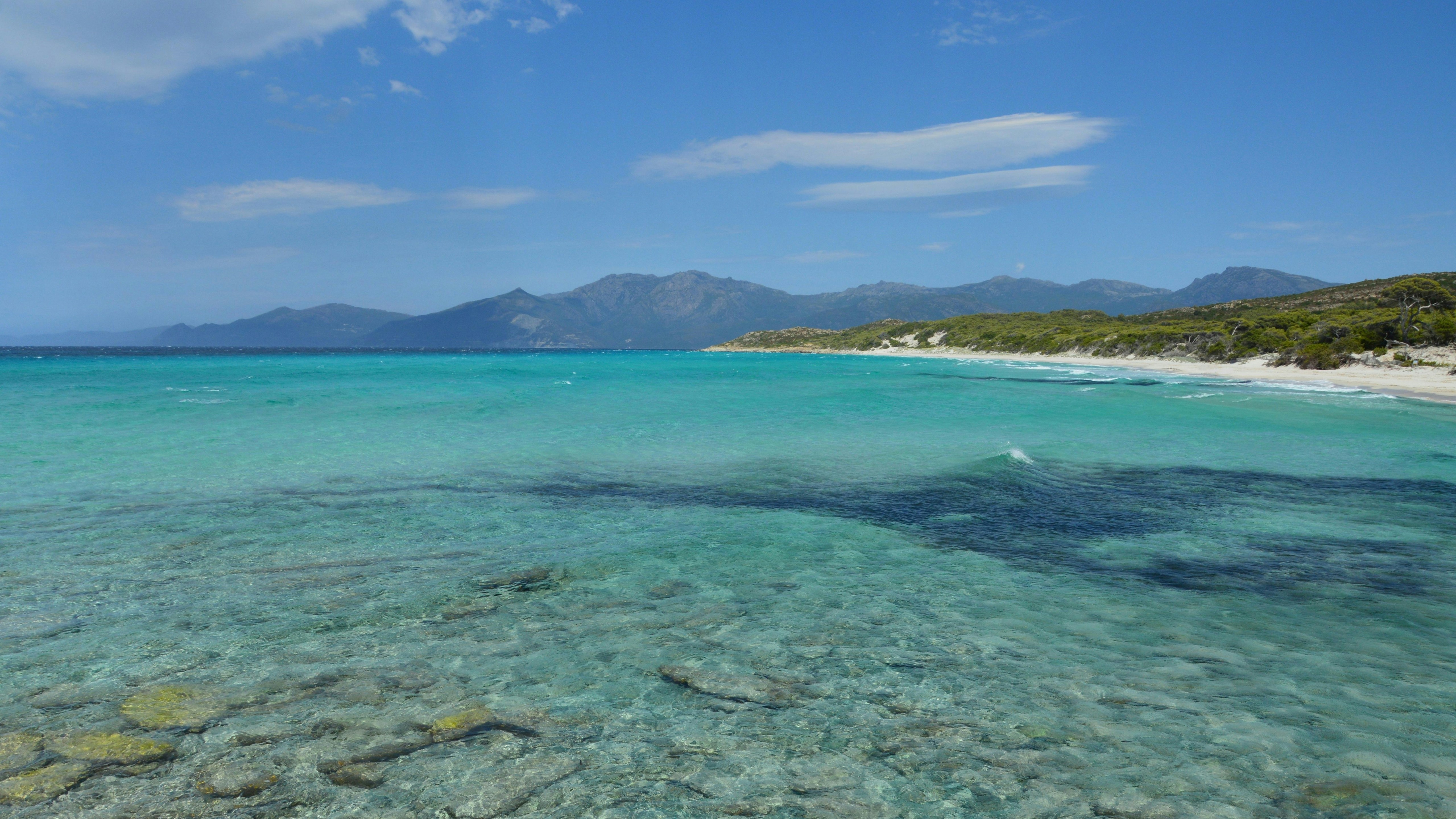 L’océan turquoise clair rencontre une plage de sable blanc et des montagnes lointaines.
