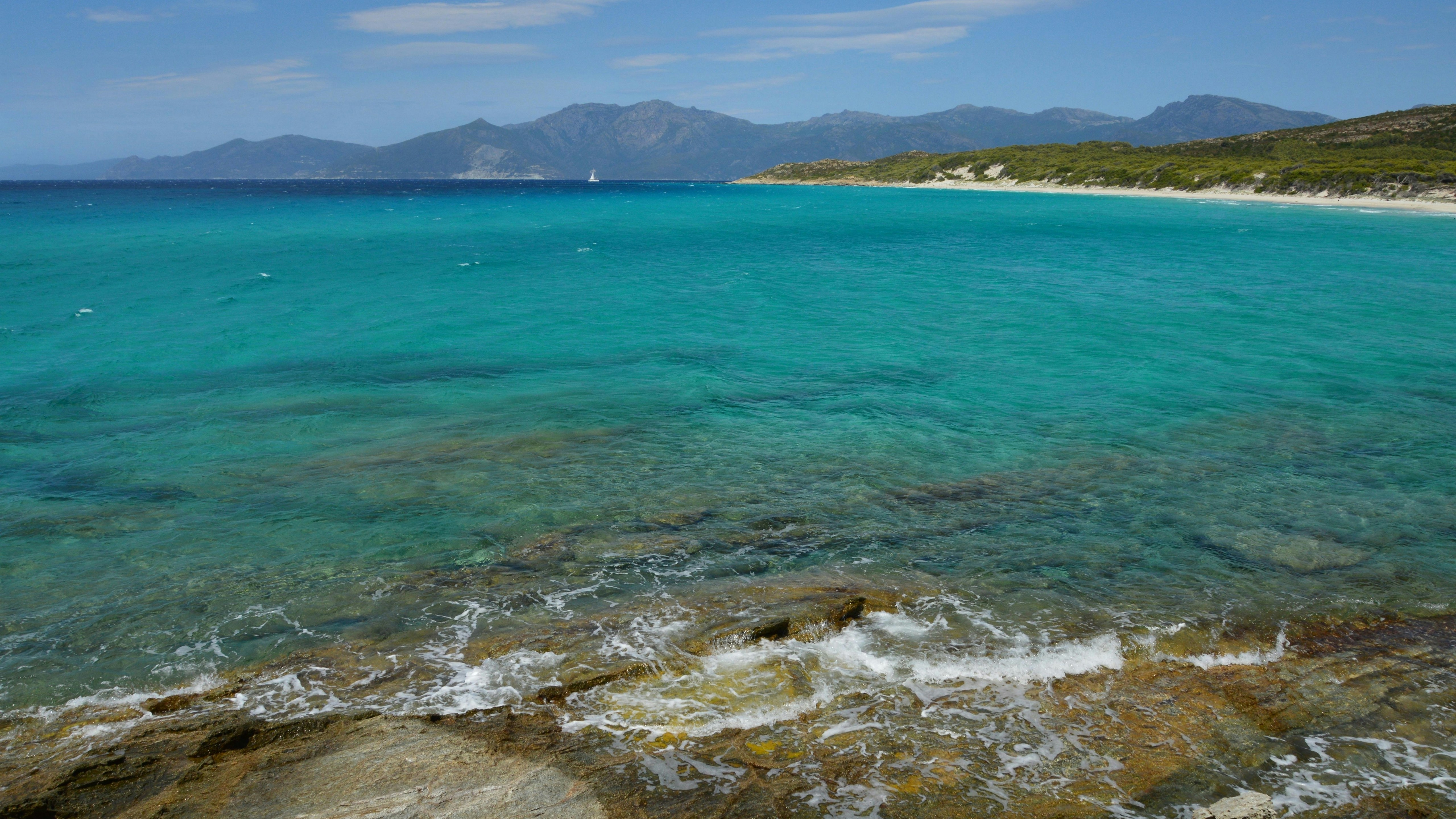 Des vagues turquoise de l’océan qui se brisent sur des rochers avec des montagnes lointaines.